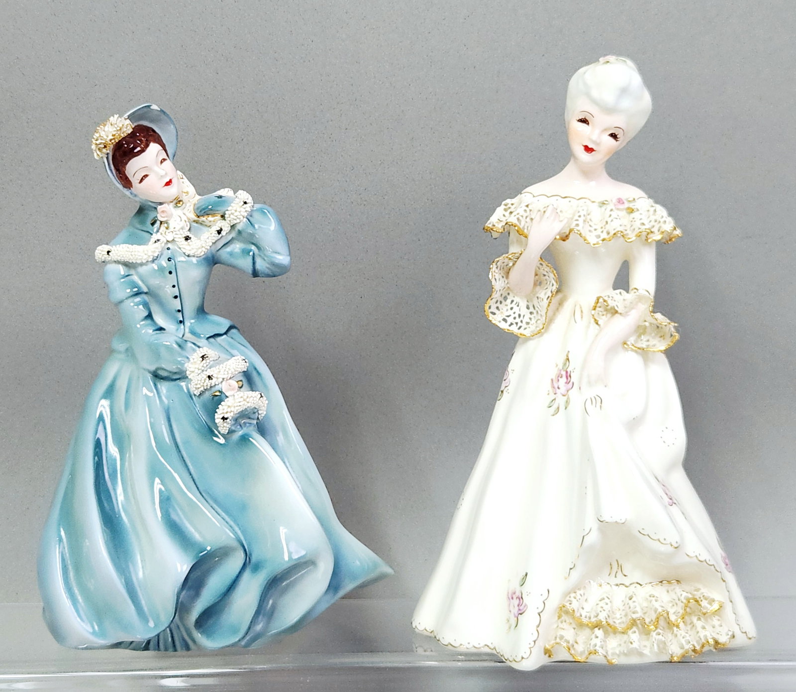 Florence Ceramics Lady Figurines: The lot includes the model Clarissa, depicted in a powder blue Victorian-style dress, model number 711. Blue figurine: Approximately 8 inches tall White figurine: Approximately 8 inches tall.