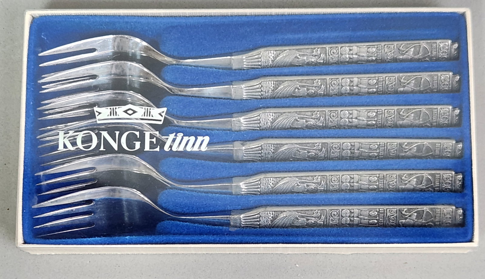 Six Konge-Tinn Norwegian Pewter Forks: This set of six Konge-Tinn pastry forks features cast pewter handles with polished stainless steel tines, presented in its original blue presentation box. The Heilag Olav pattern depicts relief-cast s