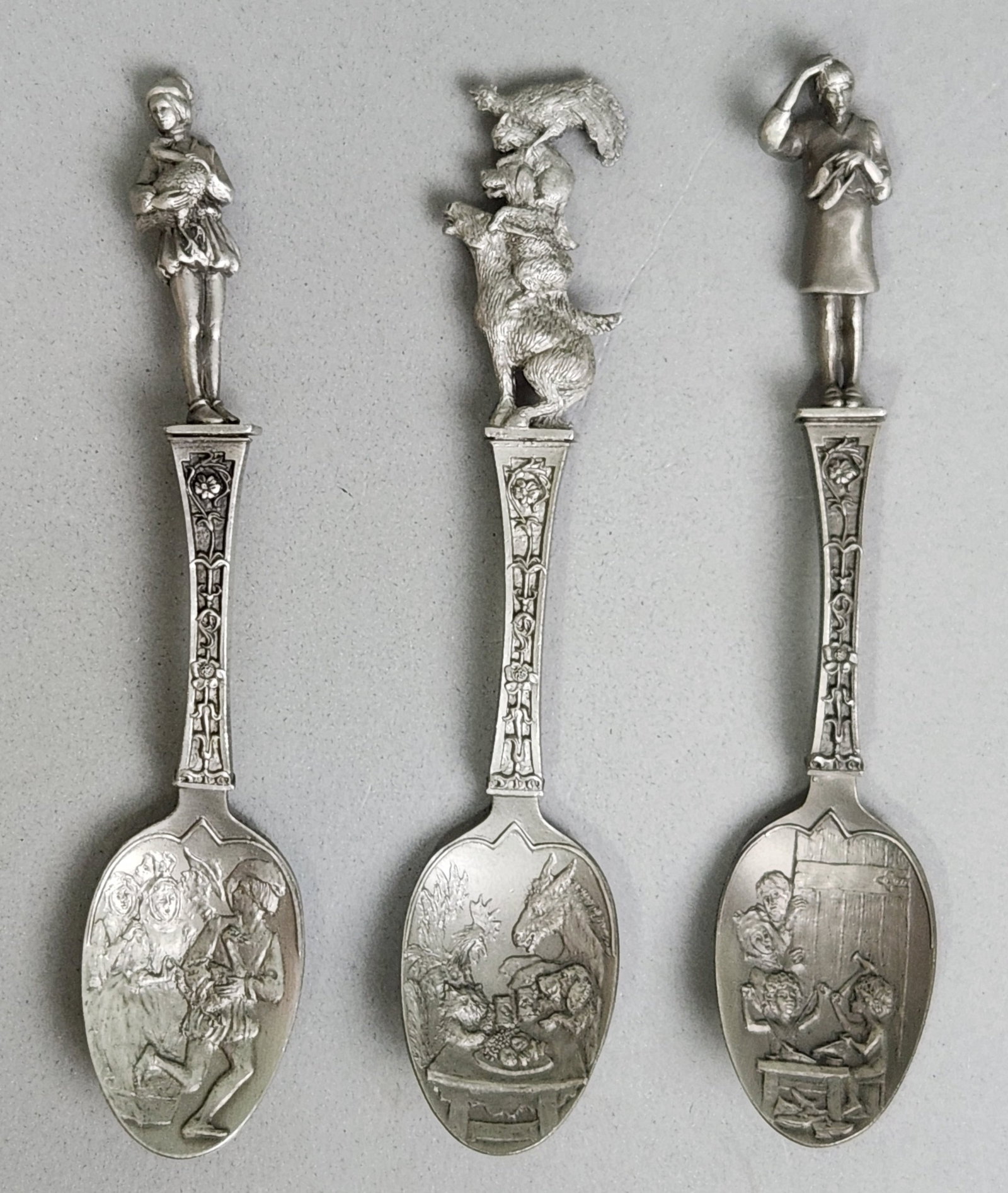 A Trio of Franklin Mint Spoons: This set of three 1979 Franklin Mint cast pewter spoons features sculptural finials and relief-decorated bowls depicting classic Brothers Grimm fairy tales. The reverse of each handle is inscribed