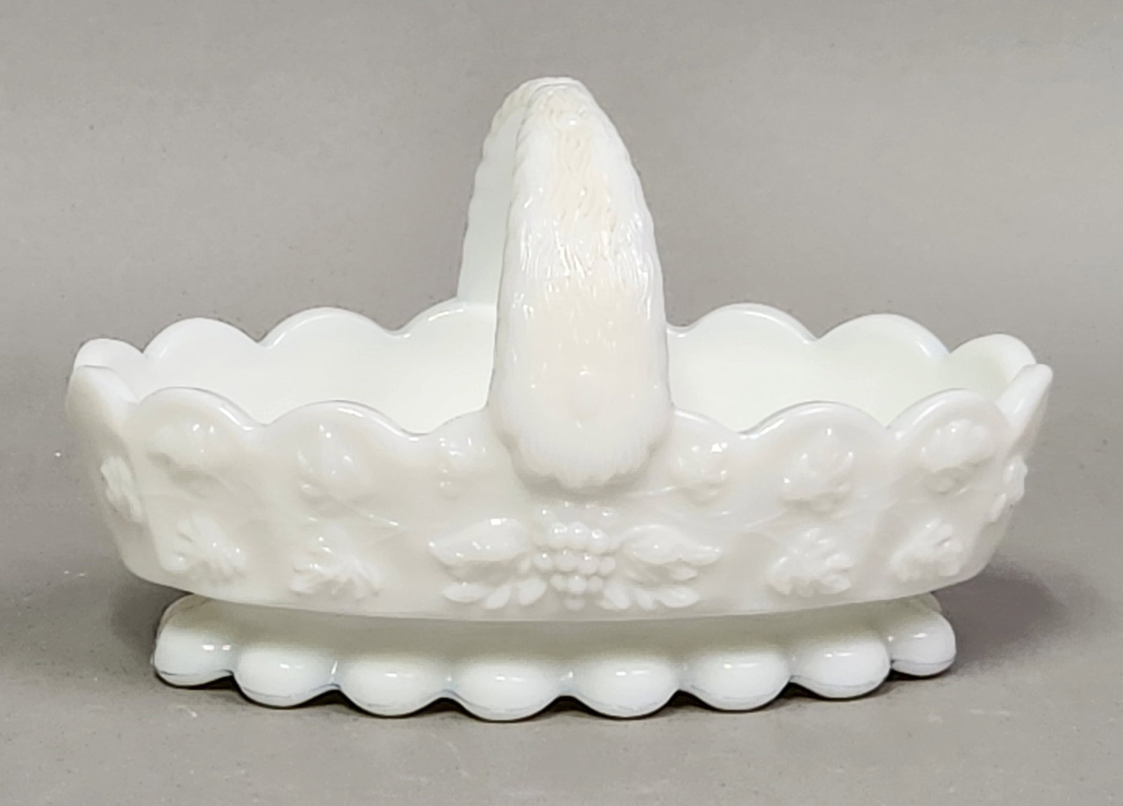 Westmoreland Milk Glass Grape Basket: A Westmoreland oval milk glass basket featuring an embossed grape and leaf relief pattern. Length: 5.5 inches Width: 3.25 inches Height: 4 inches. This piece is in excellent condition with no chips,