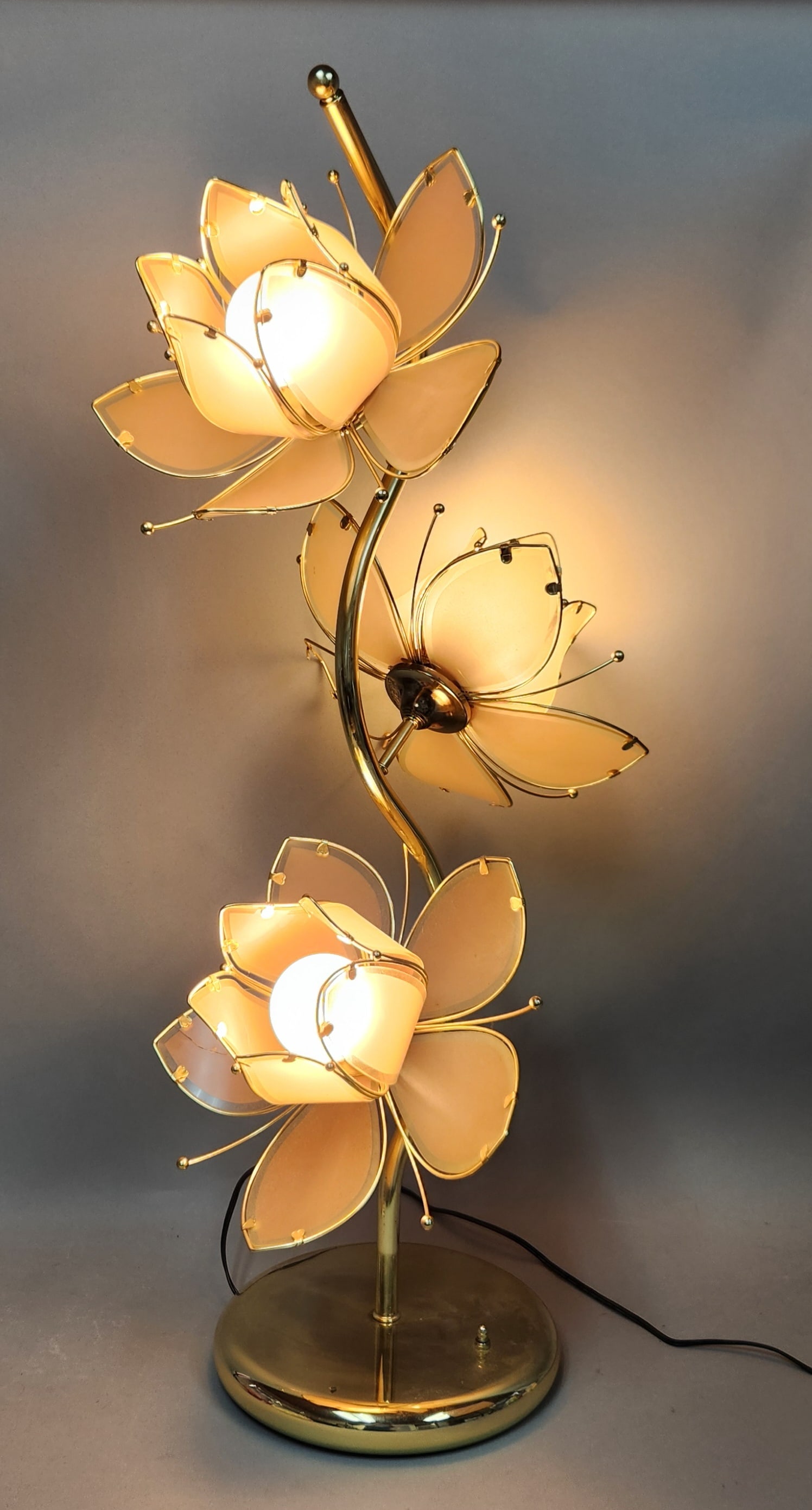 Hollywood Regency Lotus Table Lamp: A vintage three-light table lamp in the Hollywood Regency style featuring a brass-toned metal body with a central curved stem. Height: 40 inches. Damaged. One glass petal is vertically cracked and