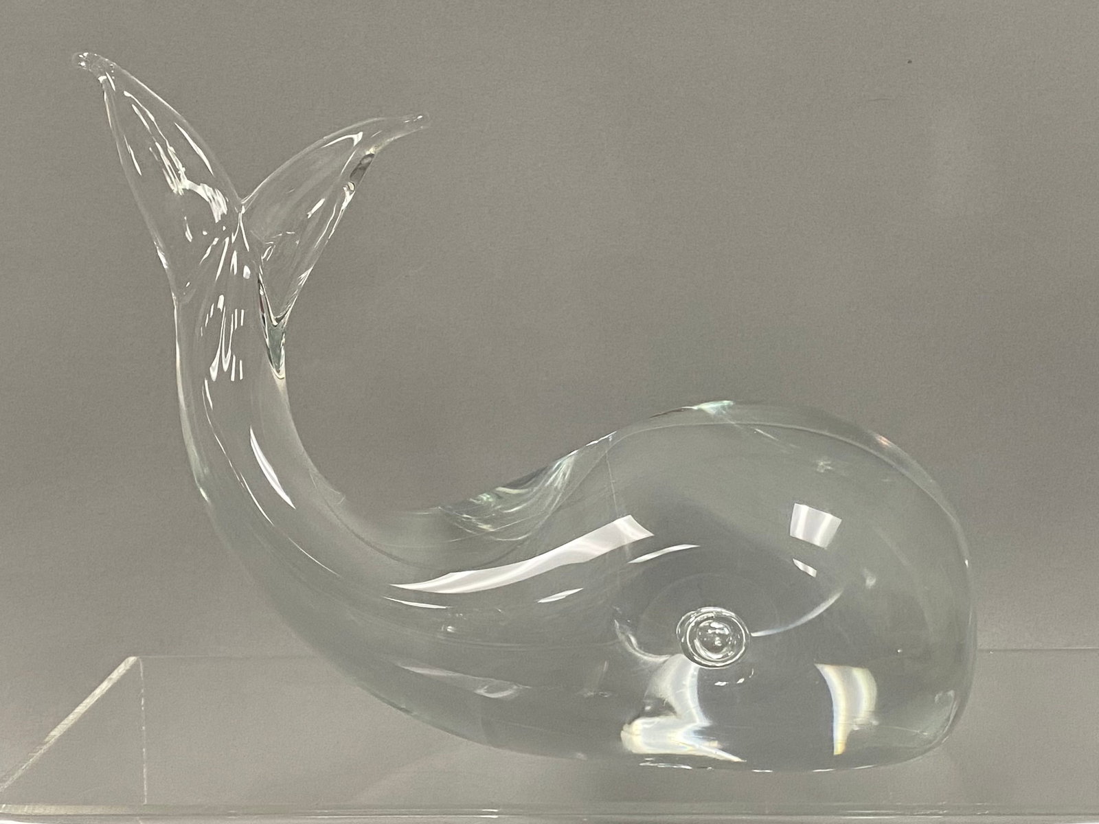 Licio Zanetti Murano Glass Whale: This clear hand-blown glass figurine in the style of Licio Zanetti depicts a stylized whale in a dynamic arched pose with an upturned tail. The sculpture features a rounded body with distinctive