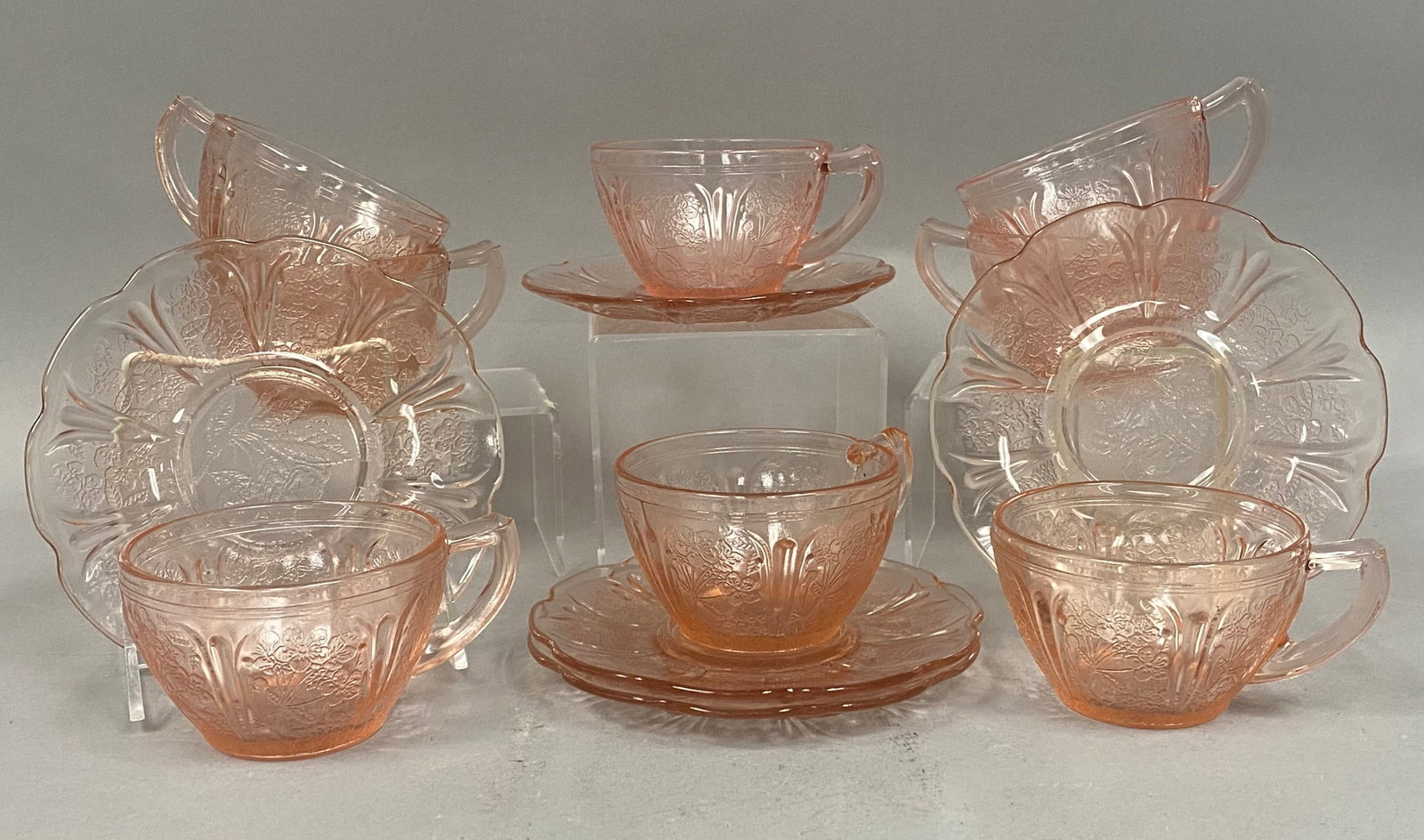 Jeannette Cherry Blossom Pink Glass Collection: This collection of thirteen pink Depression glass pieces features the Cherry Blossom pattern manufactured by the Jeannette Glass Company, comprising eight teacups and five saucers. Each piece is