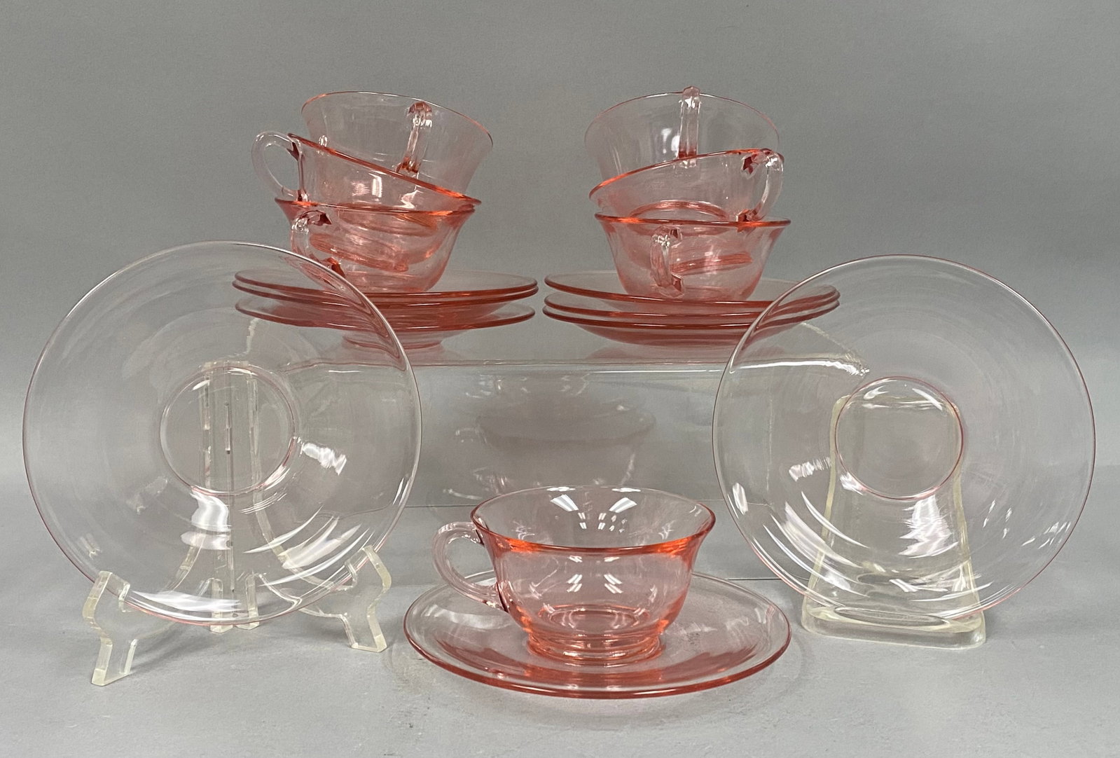 16-Piece Fostoria Pink Glass Set: A sixteen-piece set of Fostoria rose pink glass in the Fairfax pattern, comprising seven cups and nine saucers. The pieces are crafted from translucent molded glass with flared rims and curved
