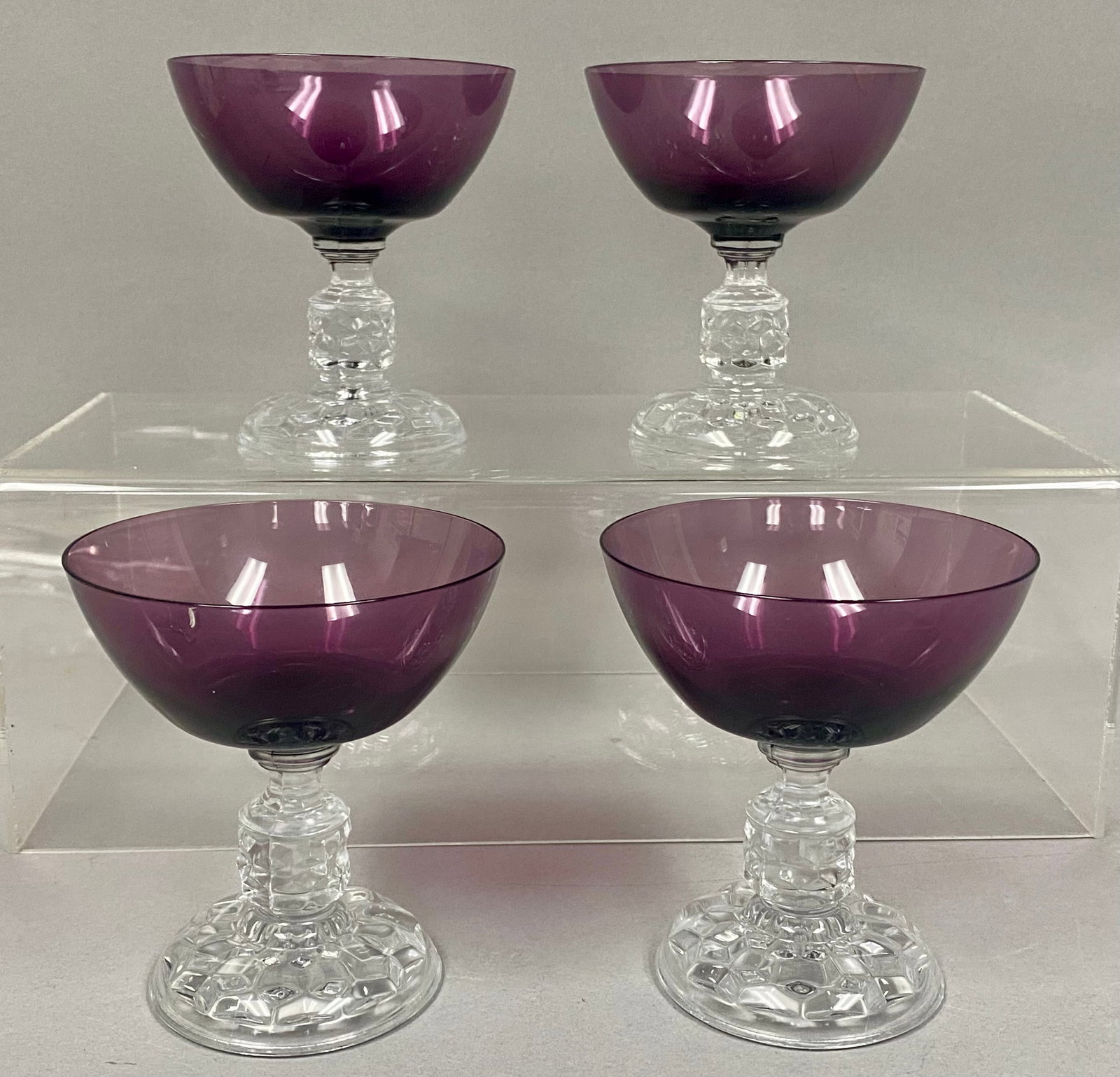 A Set of 4 Amethyst Stemware: This set of four stemware features deep amethyst purple bowls of rounded coupe form. Each piece is supported by a clear glass pedestal stem and base decorated with a molded, multi-faceted cube