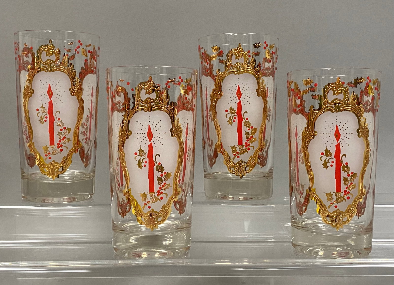 Christmas Candle Highball Glasses: This set of four clear glass highballs feature a Christmas Candle Holly pattern attributed to Culver Ltd. Each tumbler is decorated with three gold Rococo-style cartouches framing a central red
