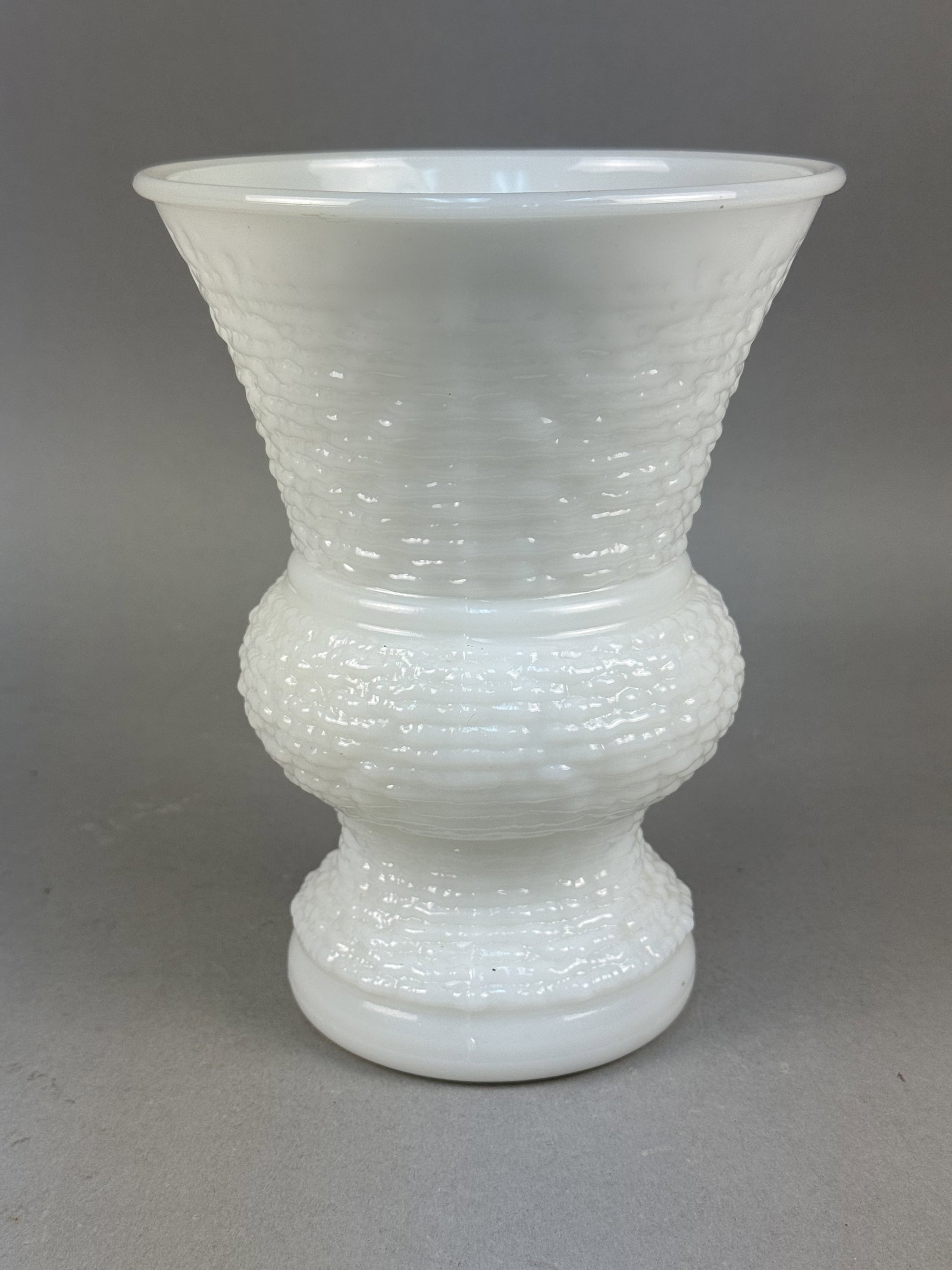 NAPCO Basketweave Milk Glass Vase: This mid-century white milk glass vase by the National Potteries Corporation features an all-over molded basketweave pattern. The flared pedestal form includes a distinctive bulbous central band and a