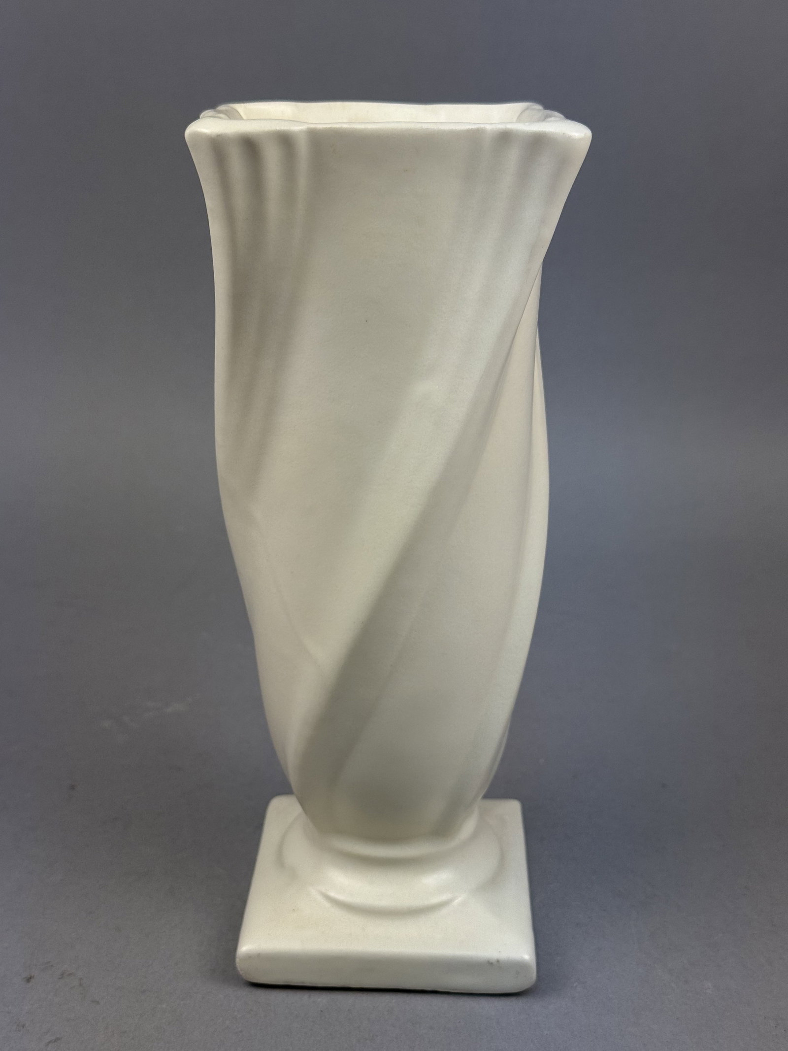 Camark Pottery Twisted Ivory Vase: A mid-century Camark Pottery earthenware vase from the Deluxe Artware line featuring a spiral-fluted trumpet form. The vessel transitions from a square, scalloped rim to a circular neck supported by