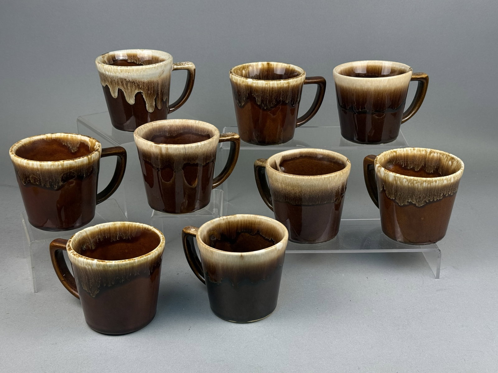 Set of Nine Ken-Craft Brown Drip Mugs: A set of nine Ken-Craft stoneware mugs featuring a tapered cylindrical form with integral D-shaped handles. Each piece is finished in a traditional brown drip glaze consisting of a chocolate-colored b