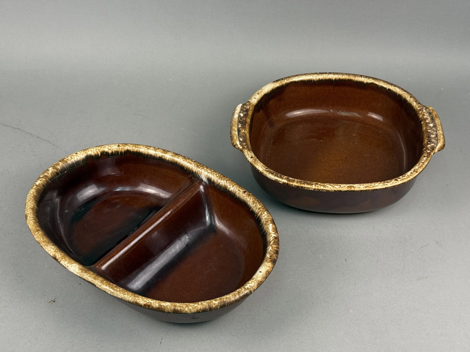 Hull Brown Drip Serving Dishes: A pair of Hull Pottery Company ovenware dishes finished in the Mirror Brown glaze pattern. The set includes a divided oval serving bowl and a rectangular-oval dish featuring integrated lug handles,
