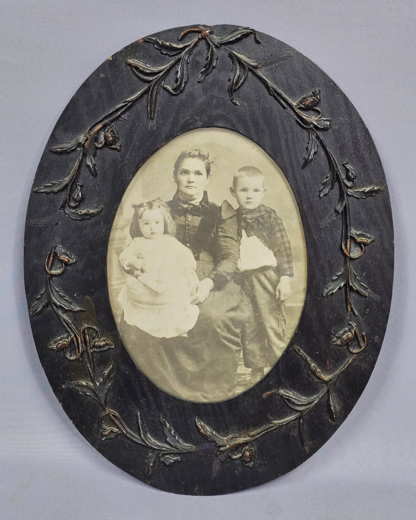 1873 Antique Wooden Framed Portrait: This monochrome portrait, likely an albumen print, depicts Viola Taylor seated with her two children. The image is set within an oval wooden frame decorated with an applied composition floral vine
