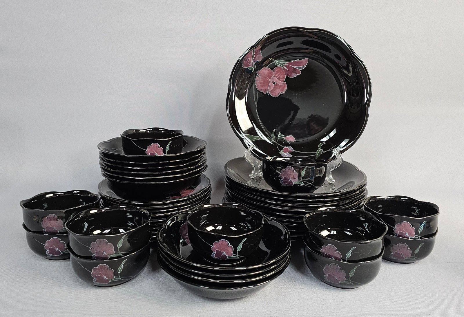 42-Piece Mikasa Tango Dinner Set: This Mikasa Rondo stoneware service in the Tango pattern features a high-gloss black glaze decorated with stylized pink and mauve floral motifs and gray-green foliage. The forms are characterized by