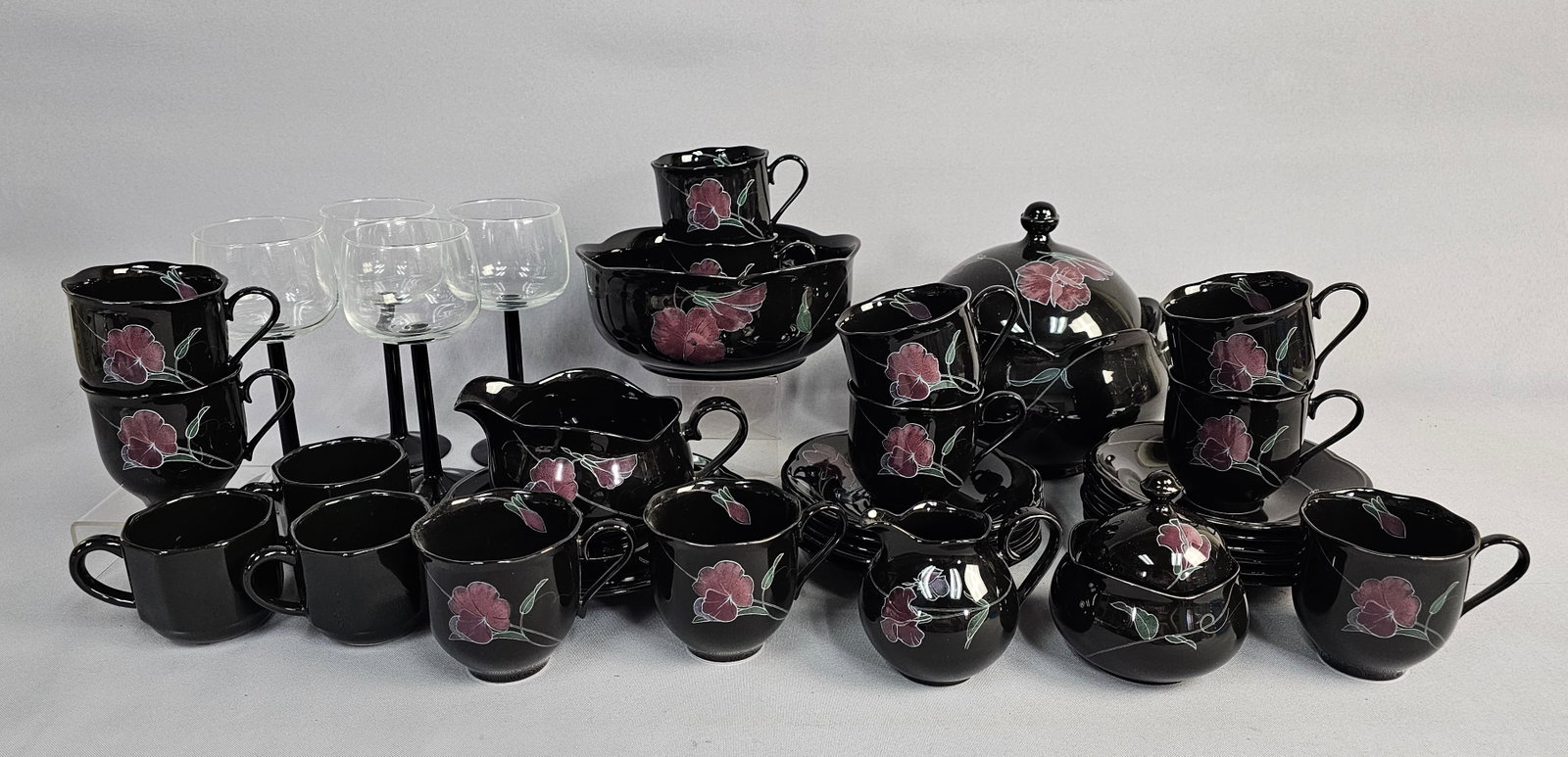 Dinnerware and Glassware Inc Mikasa Tango: The Mikasa Rondo Tango pattern pieces feature a high-gloss black ceramic ground decorated with stylized floral lily transfers in shades of pink, purple, and green. The lot includes 11 tea cups, 3