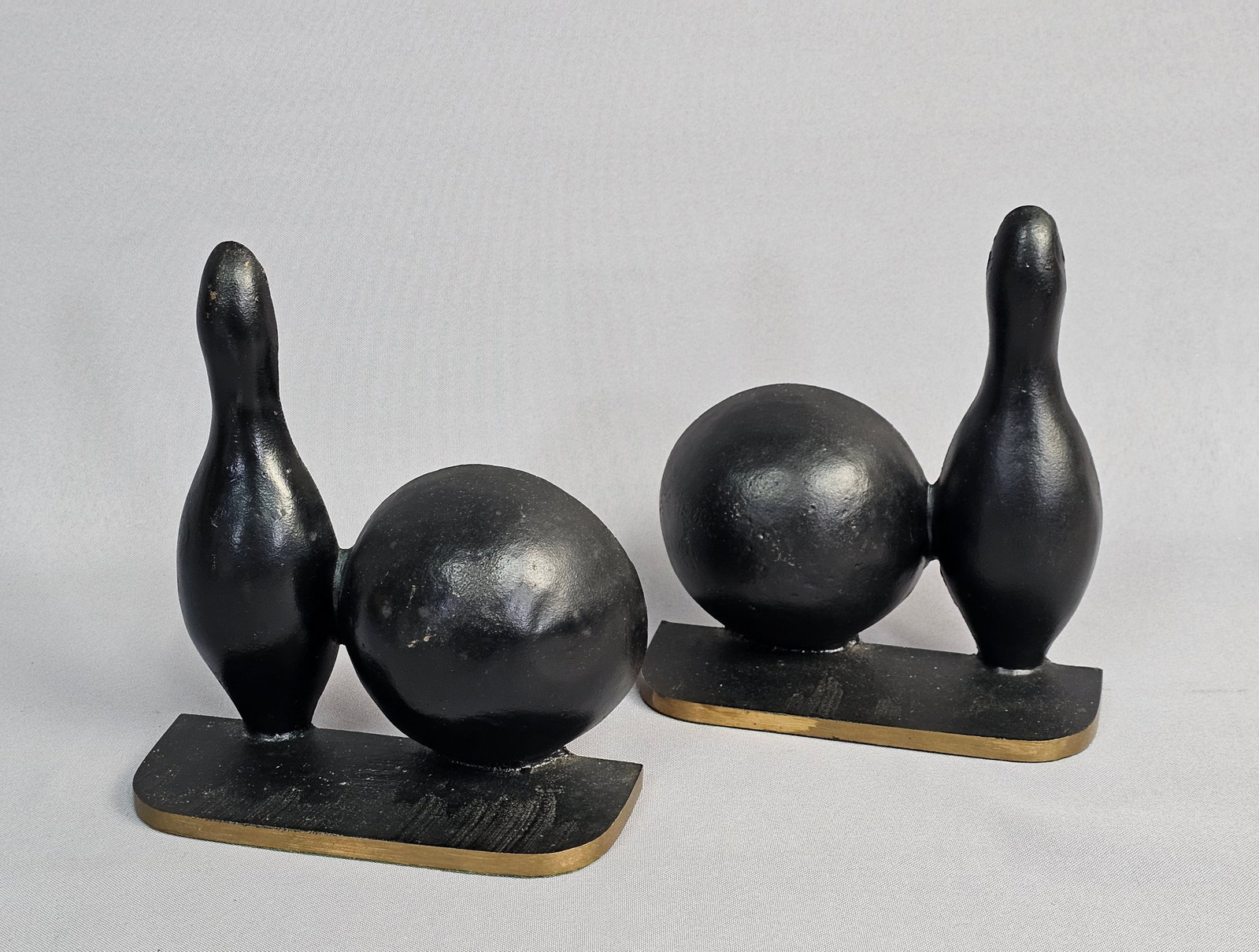 Pair of Brass Bowling Pin and Ball Bookends: This pair of solid cast brass bookends was manufactured by Brisk Foundry in Imlay City, Michigan, during the 1950s. The design features a bowling pin and ball finished in black paint on a D-shaped bas