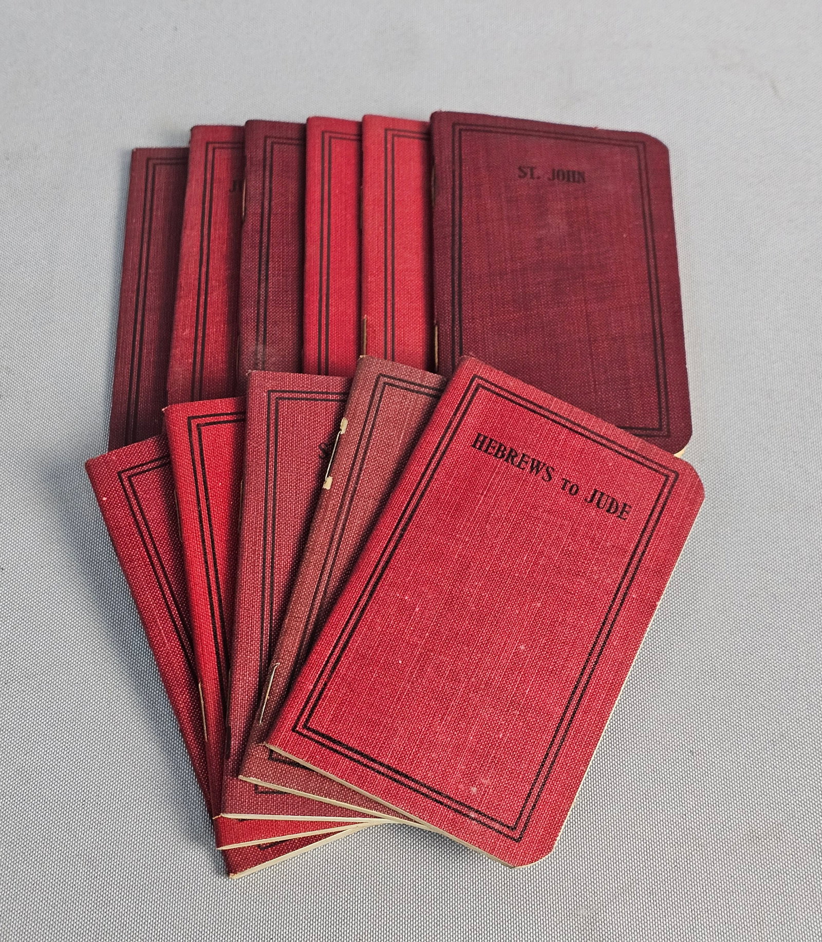 11 American Bible Society Pocket Bible Volumes: An assortment of early 20th-century pocket-sized biblical volumes published by the American Bible Society. Each staple-bound booklet features red textured wrappers with decorative black borders and