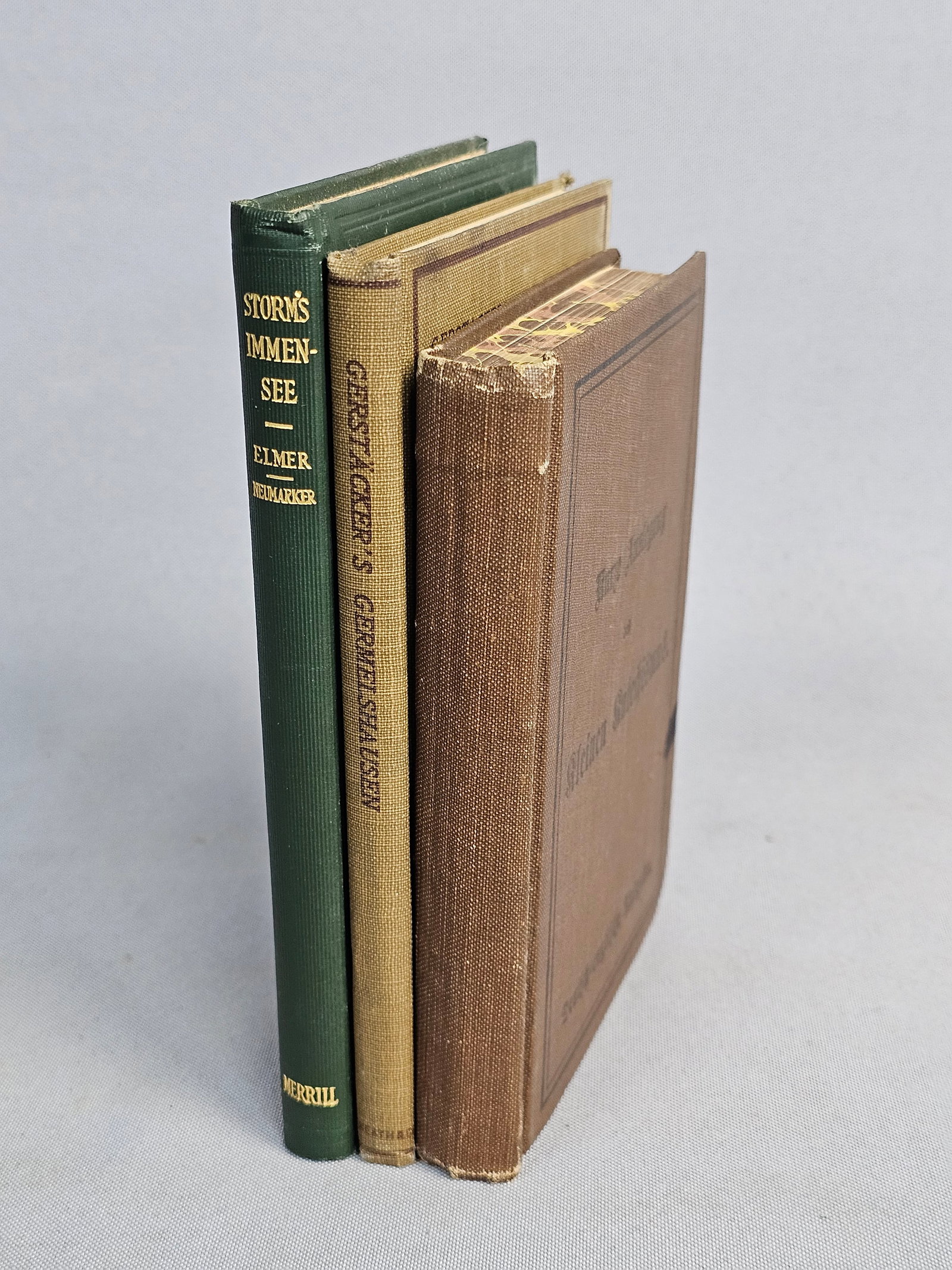 Trio of Antique German Books: This collection includes a 1909 bilingual edition of Luther's Small Catechism, Friedrich Gerstacker's Germelshausen from 1902, and Theodor Storm's Immensee dated 1912. The volumes are bound in brown,