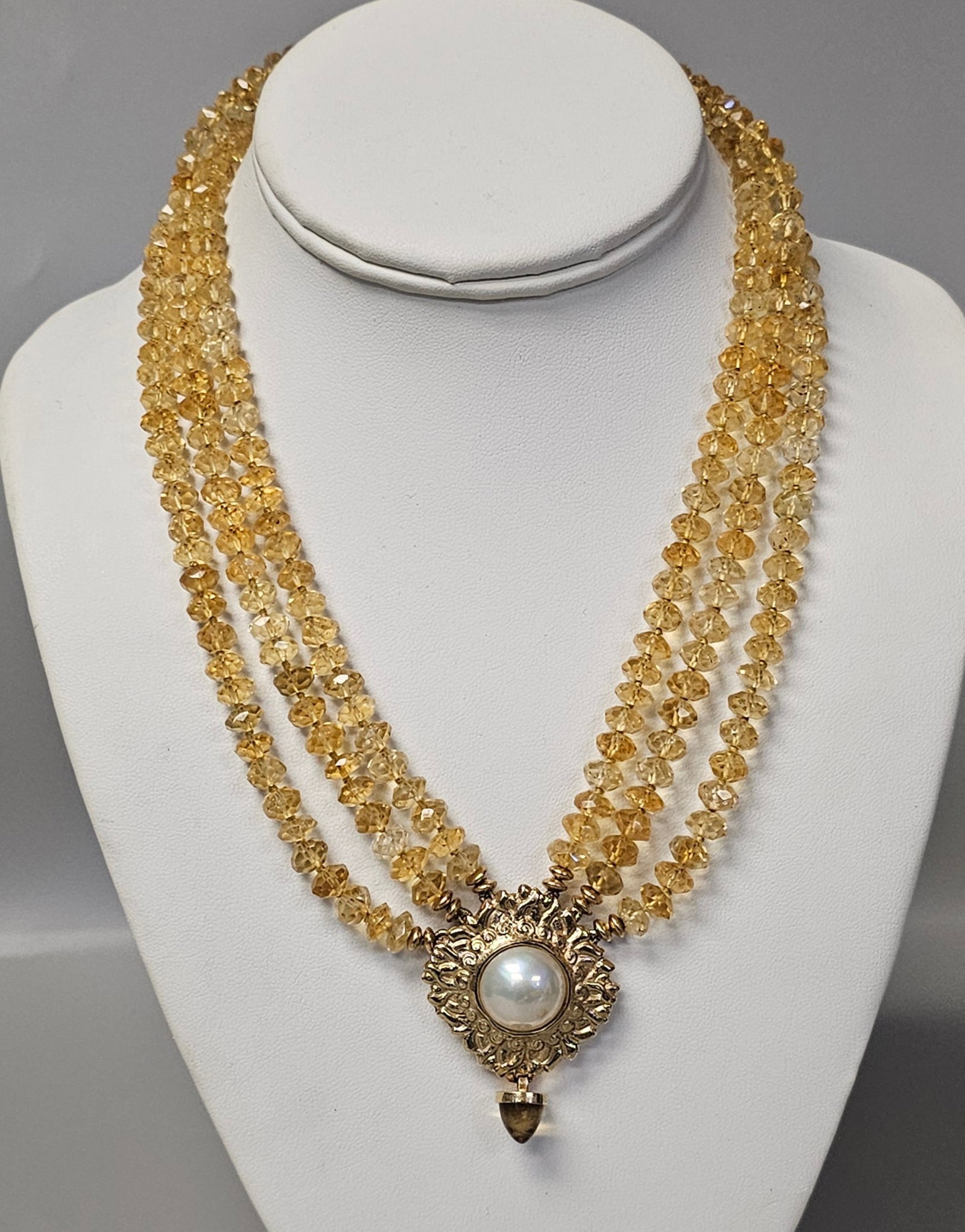 14K Citrine and Mabe Pearl Necklace: This triple-strand necklace features hand-knotted faceted citrine rondelle beads leading to a central 14 karat yellow gold pendant with an ornate scrollwork border. The pendant is set with a large 16m