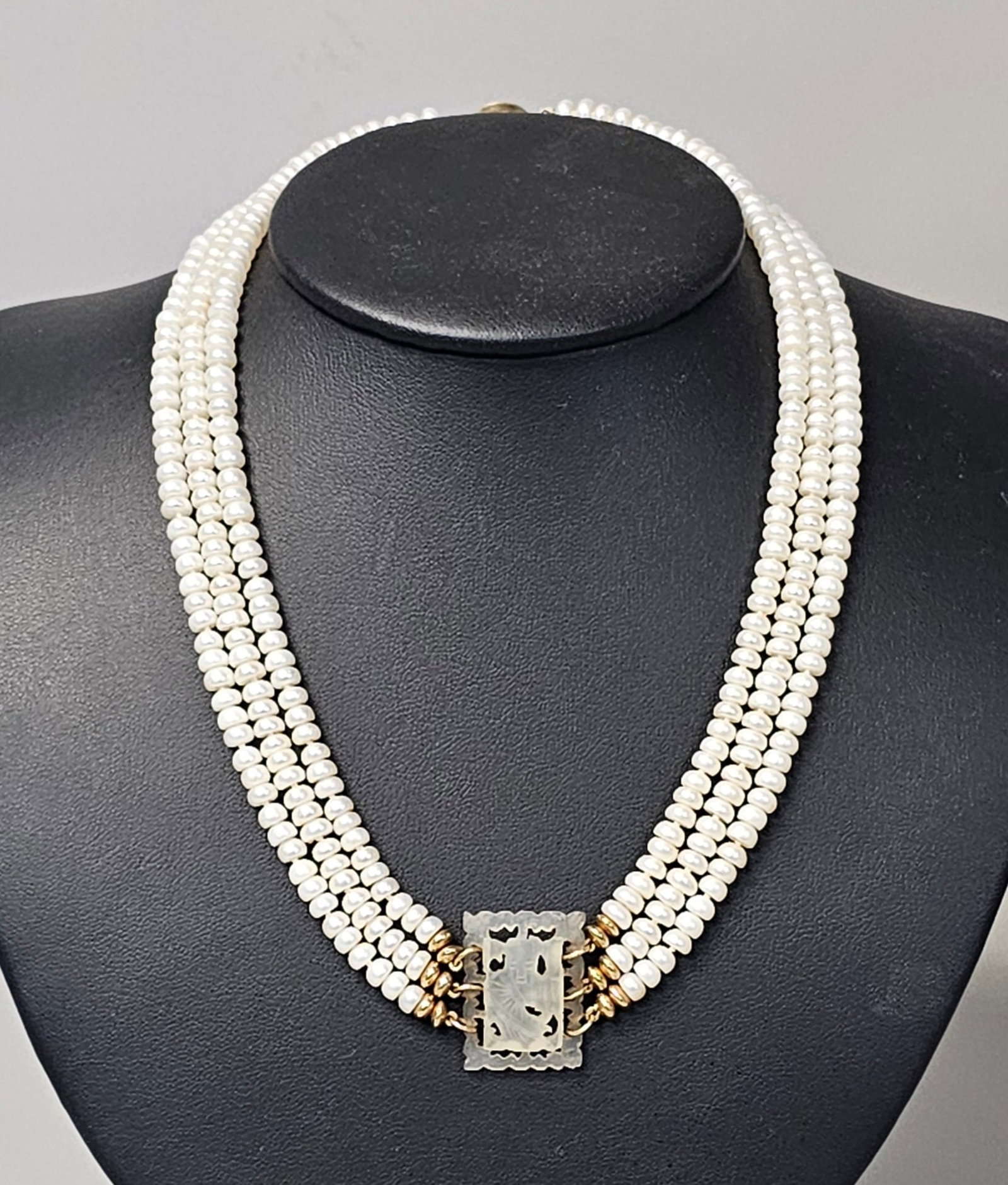14K Triple-Strand Pearl and Carved Jade Necklace: This late 20th-century necklace features three strands of creamy white cultured pearls centered by an intricately pierce-carved translucent jade plaque. The piece is constructed with 14-karat yellow g