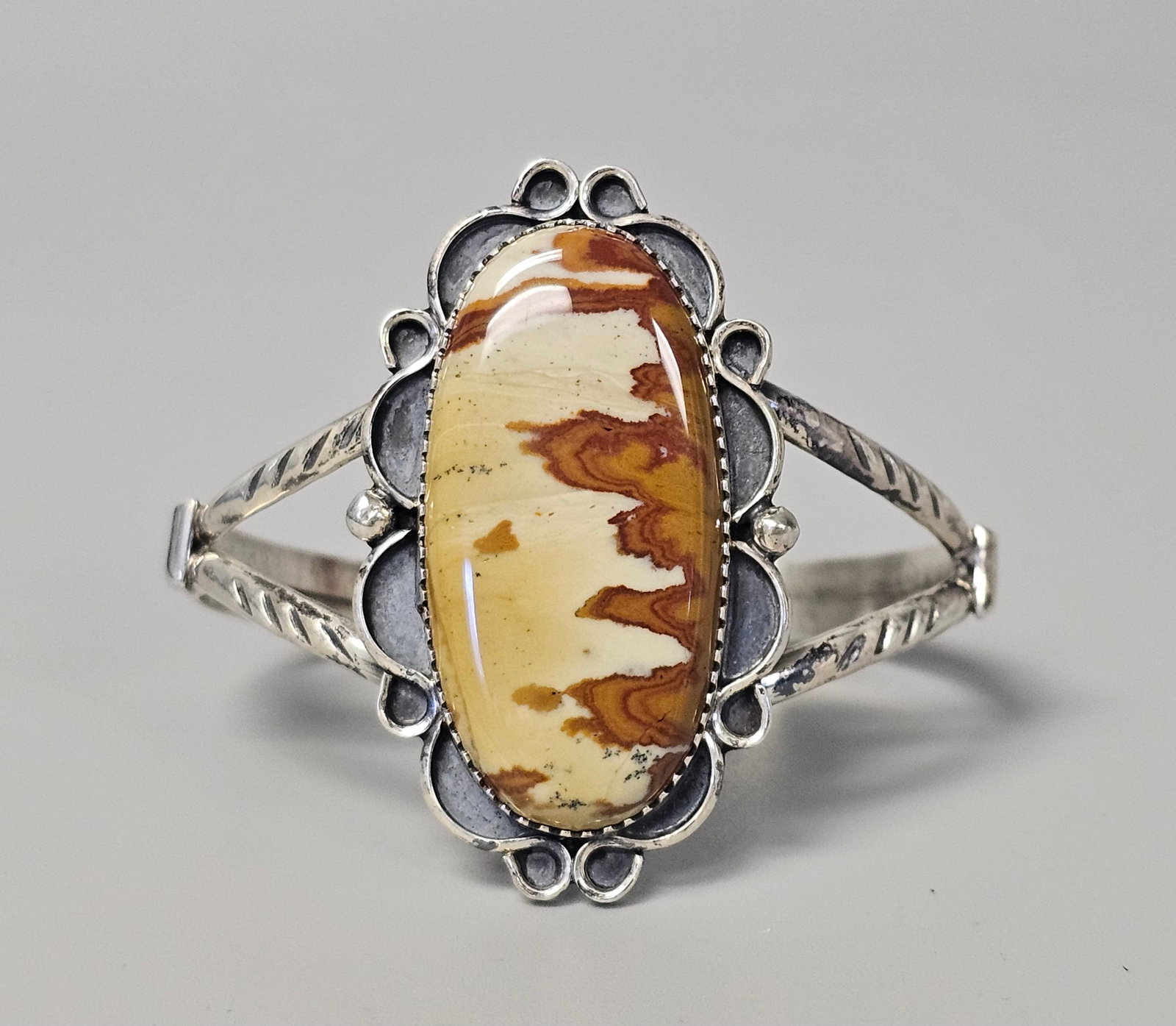 Sterling Southwestern Picture Jasper Cuff 28.2 Grams: A Southwestern-style split-shank cuff bracelet featuring a large oval picture jasper cabochon with a scenic landscape pattern. The 28.2-gram piece is detailed with a sawtooth bezel and scalloped silve