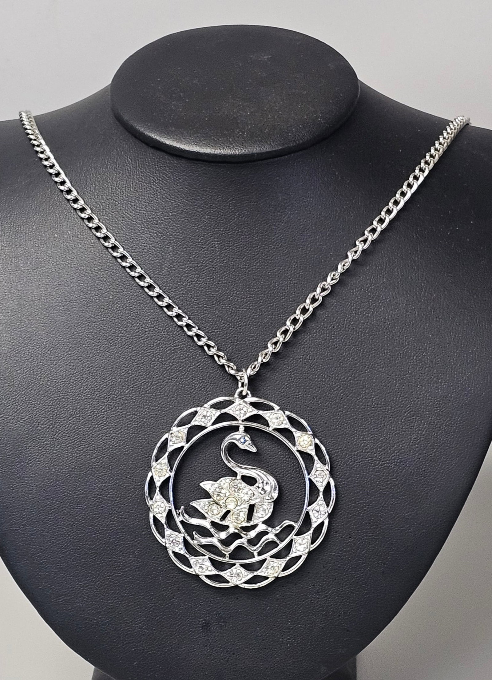 Sarah Coventry Swan Pendant Necklace: A vintage silver-tone necklace featuring a large circular openwork pendant with a rhinestone-accented swan motif. The pendant measures approximately 2.25 inches in diameter and is suspended from a 28-