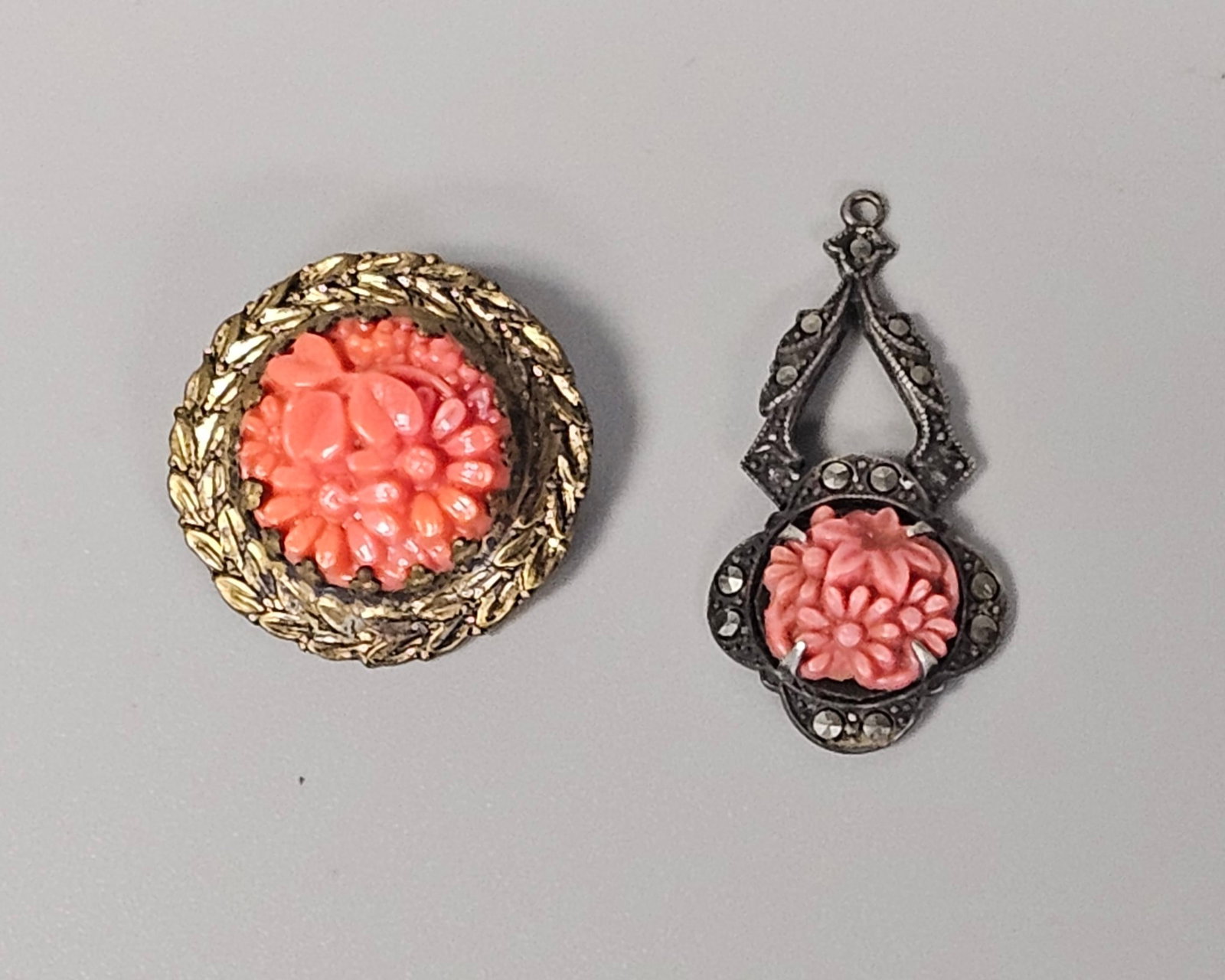 Two Carved Floral Jewelry Pieces: This lot features a sterling silver teardrop pendant with an Art Deco openwork frame, marcasite stones, and a central carved floral motif. It is paired with a circular gold-tone brooch displaying a ca