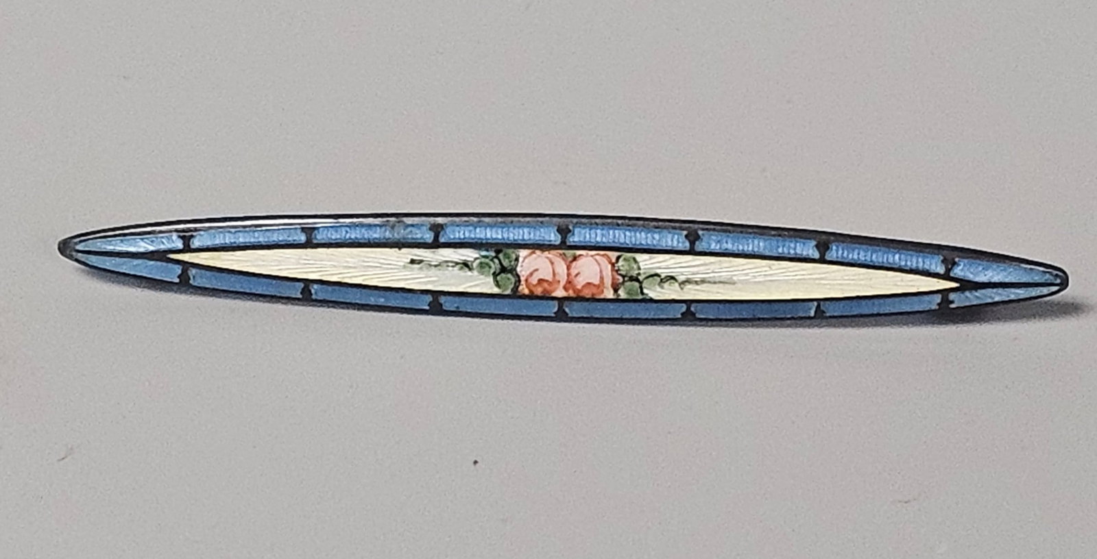 Art Deco Enamel Bar Brooch: This sterling silver bar brooch features a central marquise-shaped panel of white guilloche enamel decorated with hand-painted pink roses. The Art Deco period piece is bordered by a segmented band of 