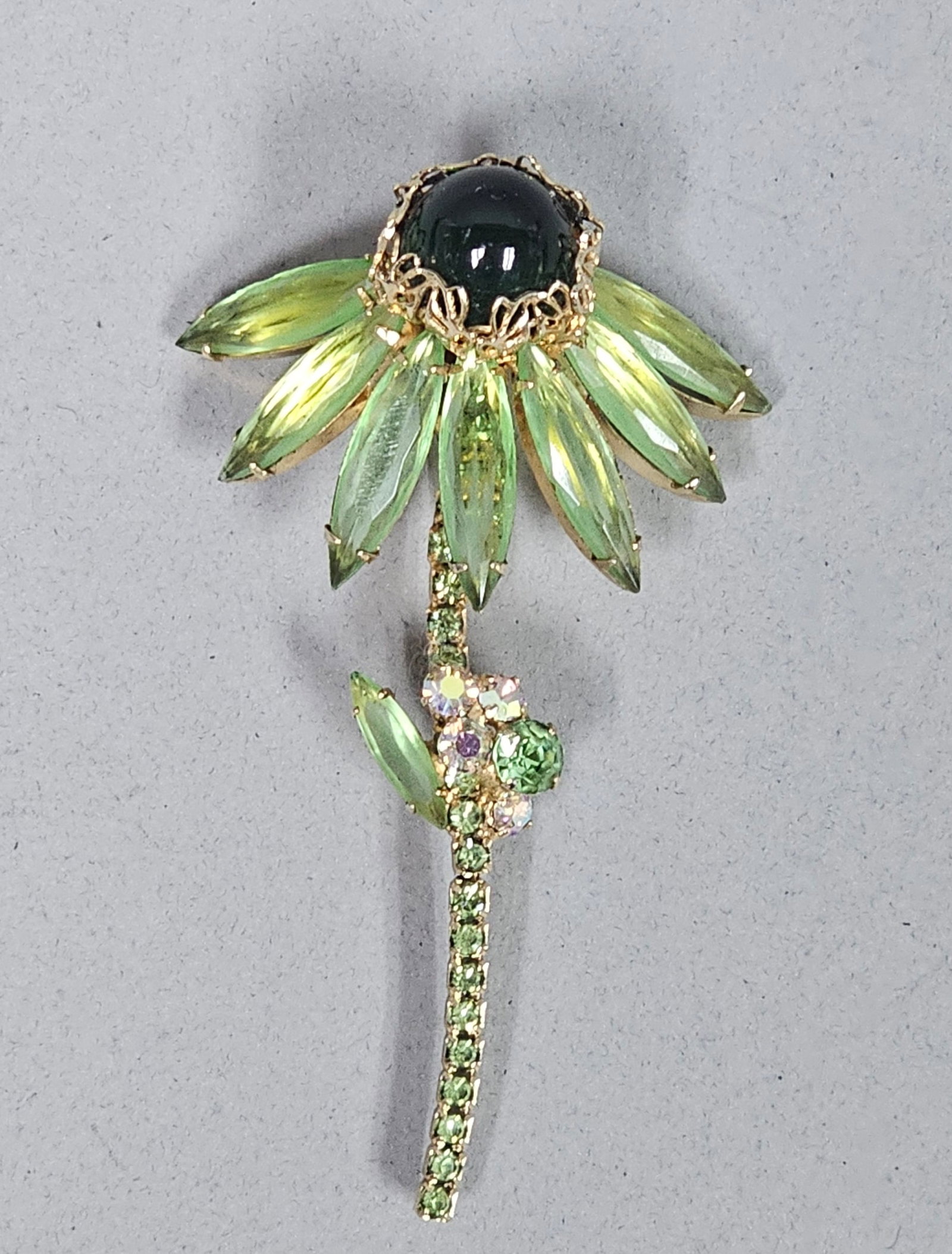 Vintage Green Rhinestone Floral Brooch: This vintage floral spray brooch is designed in the form of a coneflower featuring a large dark green glass cabochon centerpiece in a filigree setting. The petals are comprised of eight marquise-cut l
