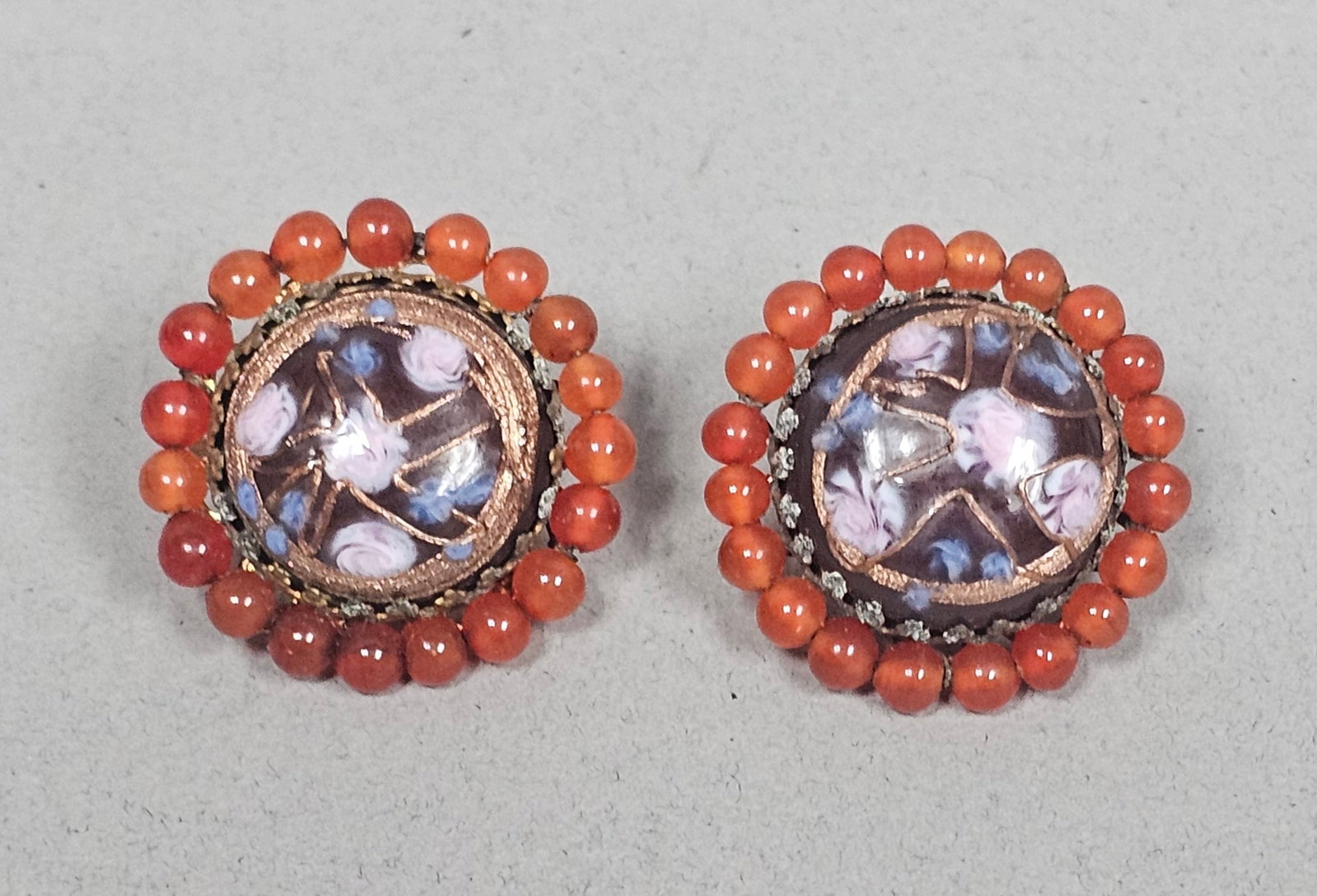 Ornella Italy Beaded Millefiori Earrings: A pair of vintage Ornella Italy clip-on earrings featuring central domed millefiori art glass cabochons with internal floral designs in shades of pink, blue, and white. The glass is bordered by a halo