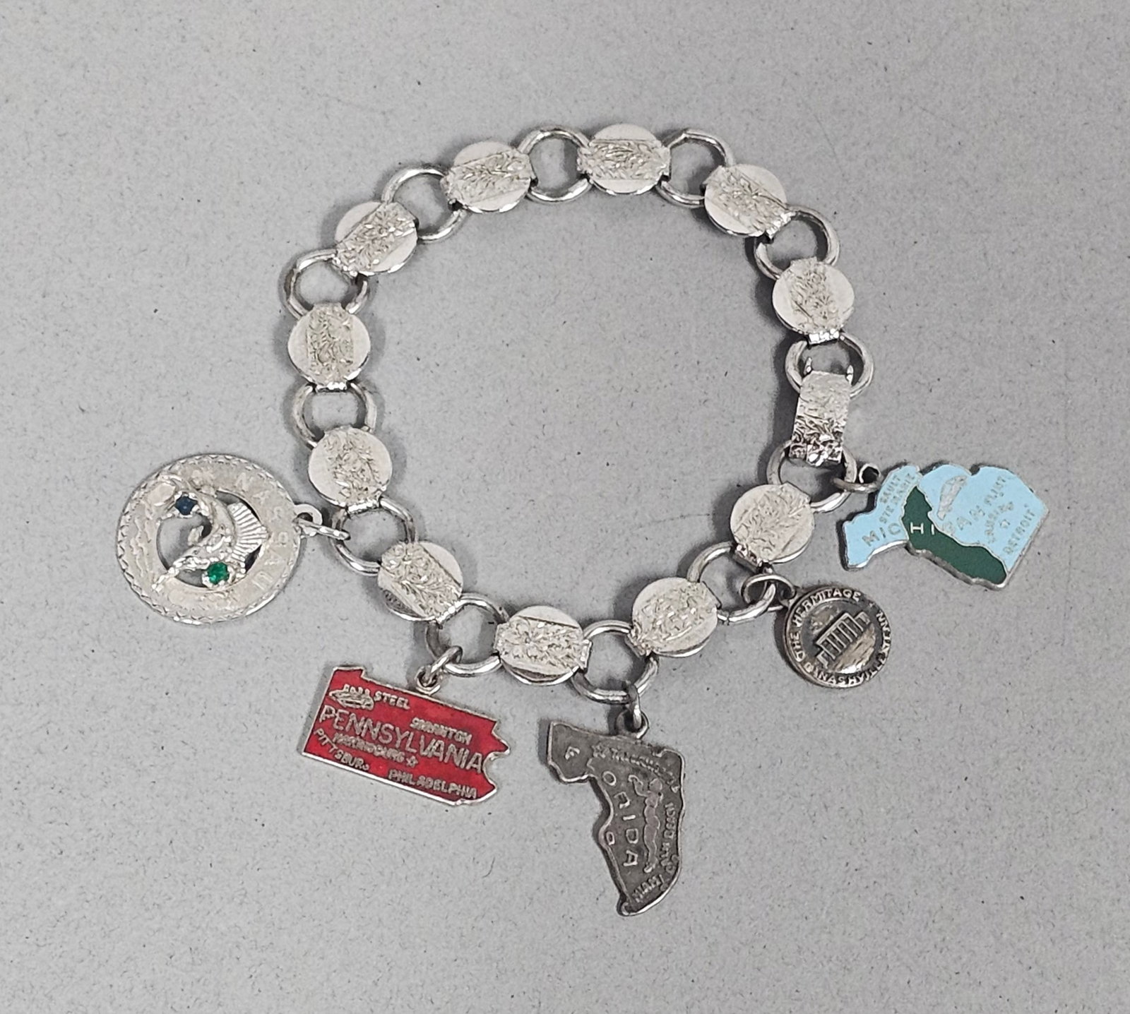 Sarah Coventry Bracelet with Sterling Charms: A vintage Sarah Coventry silver-toned link bracelet featuring five attached sterling silver souvenir charms. The collection includes map-shaped charms for Pennsylvania, Florida, and Michigan, along wi