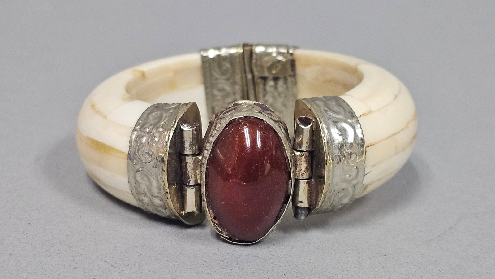 Bone and Carnelian Hinged Bangle: This silver-tone hinged bangle features a central oval carnelian cabochon set within decorative repousse metalwork. The body of the bracelet is constructed from rectangular cream-colored bone segments