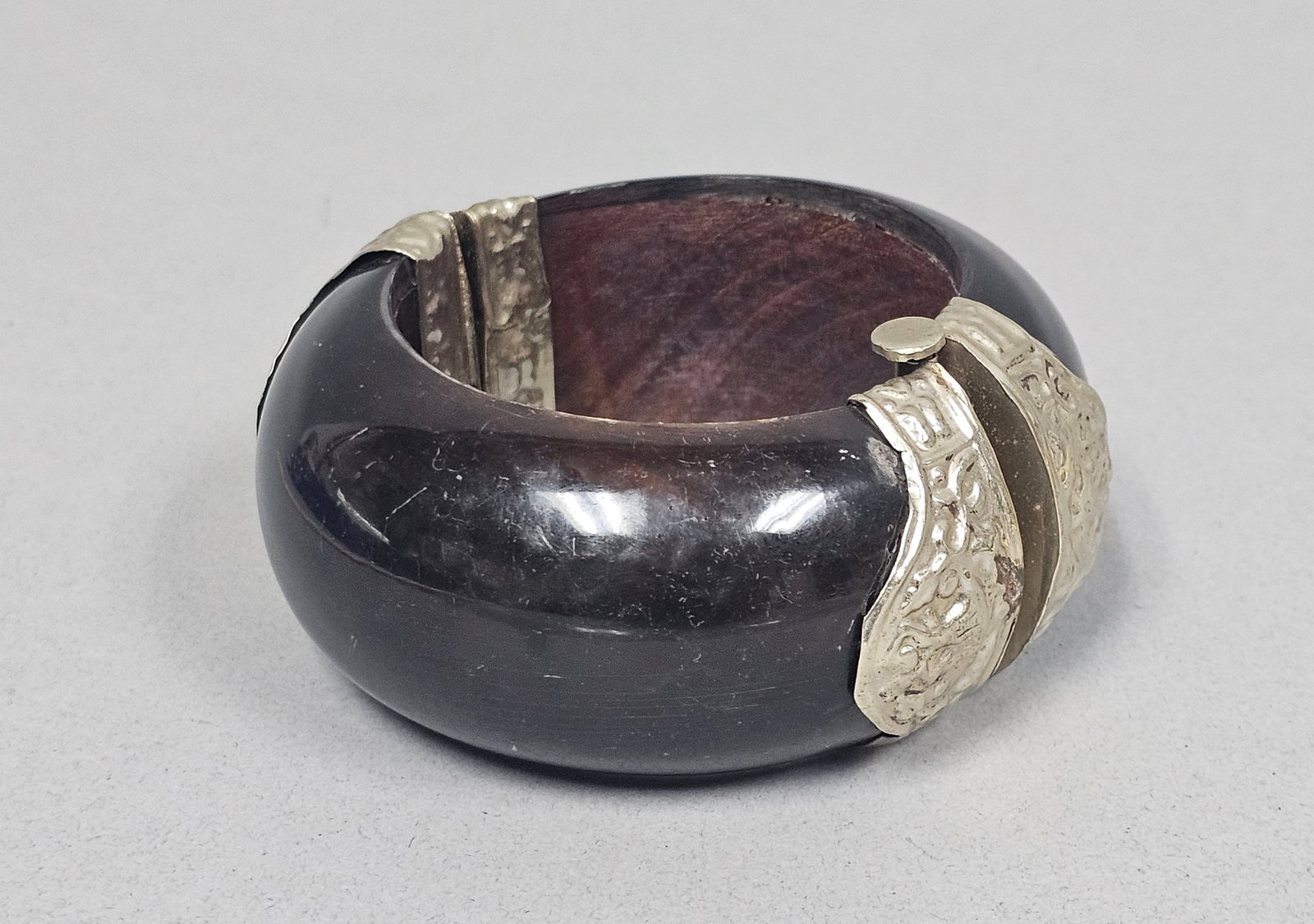Mexican Sterling Silver and Wood Bangle: A mid-century Mexican modernist hinged bangle featuring polished dark hardwood and embossed silver metal. The decorative metal hinge and clasp covers display repouss?© foliate and floral patterns. St
