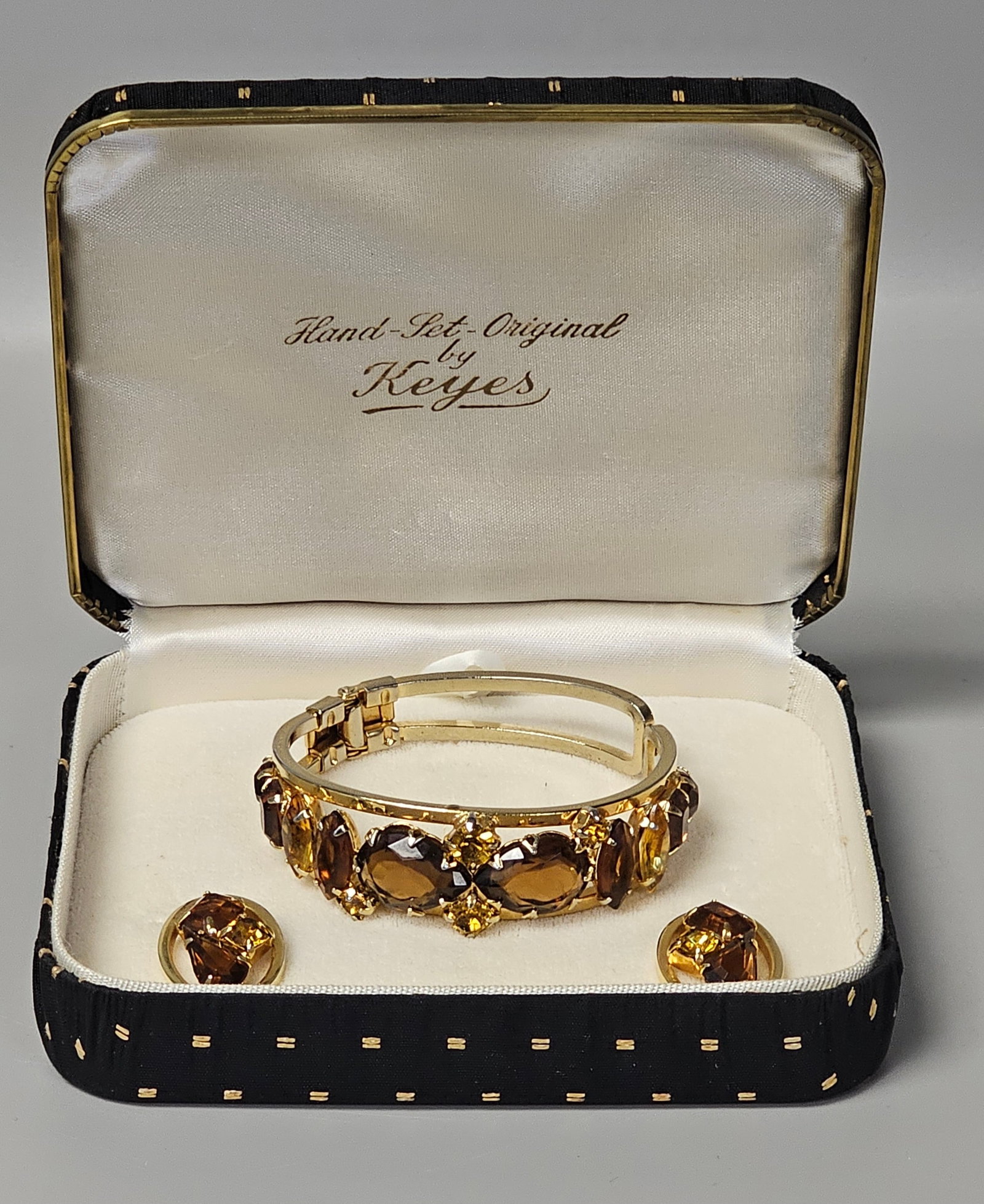 Keyes Hand-Set Rhinestone Jewelry Set: A vintage mid-century costume jewelry suite by Keyes featuring a hinged clamper bracelet and matching clip-on earrings. The gold-tone metal settings house a variety of hand-set faceted glass stones