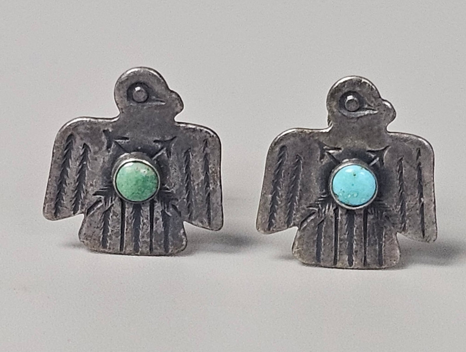 Vintage Sterling Silver Thunderbird Earrings 5.2 Grams: A pair of mid-century Southwestern sterling silver screw-back earrings fashioned in the Thunderbird motif. Each earring is decorated with stamped arrow and feather patterns and inset with a natural
