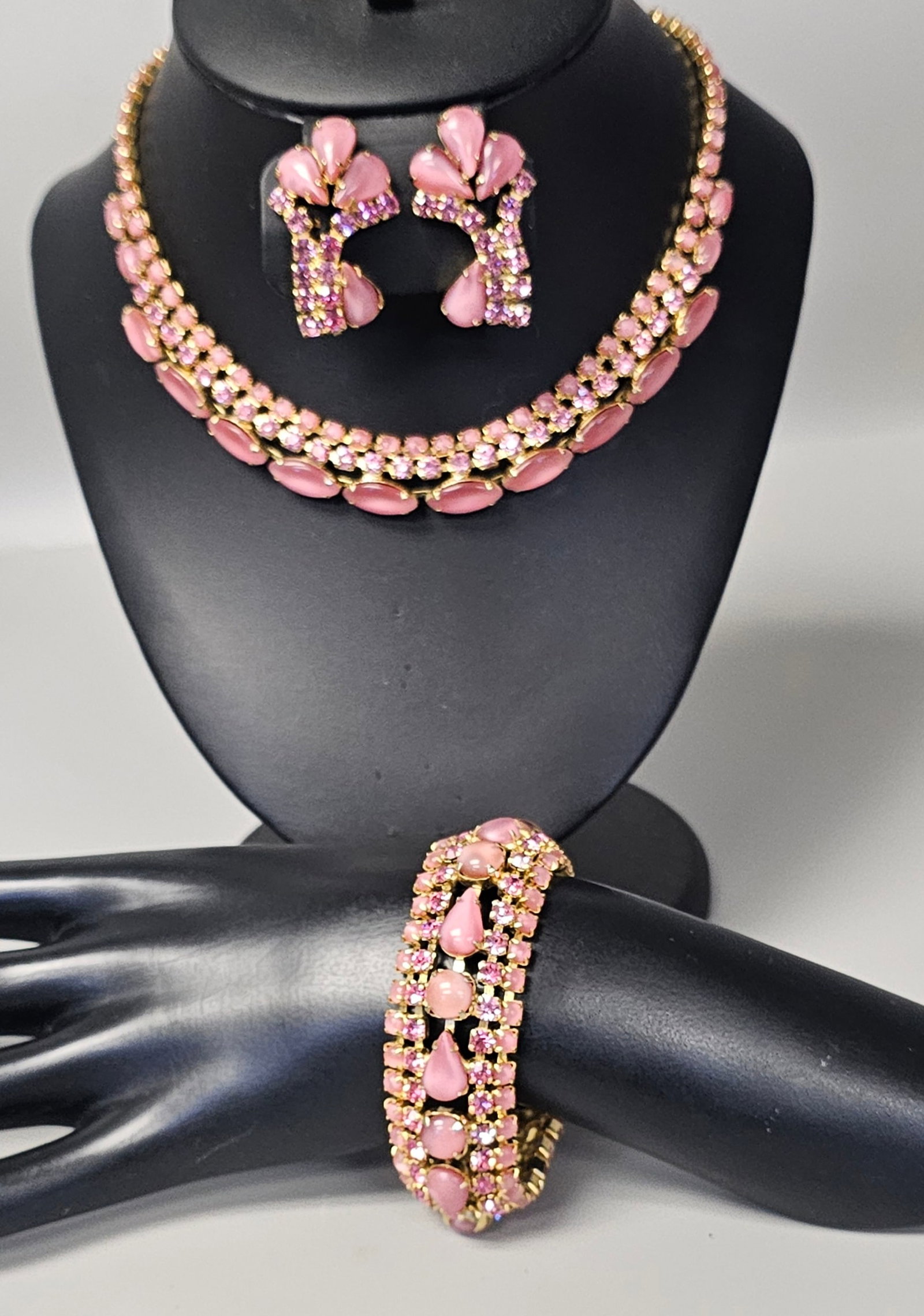 Vintage Pink Moonglow Jewelry Parure: This three-piece costume jewelry parure consists of a collar necklace, a wide link bracelet, and clip-on earrings. The set is constructed from gold-tone base metal embellished with prong-set pink