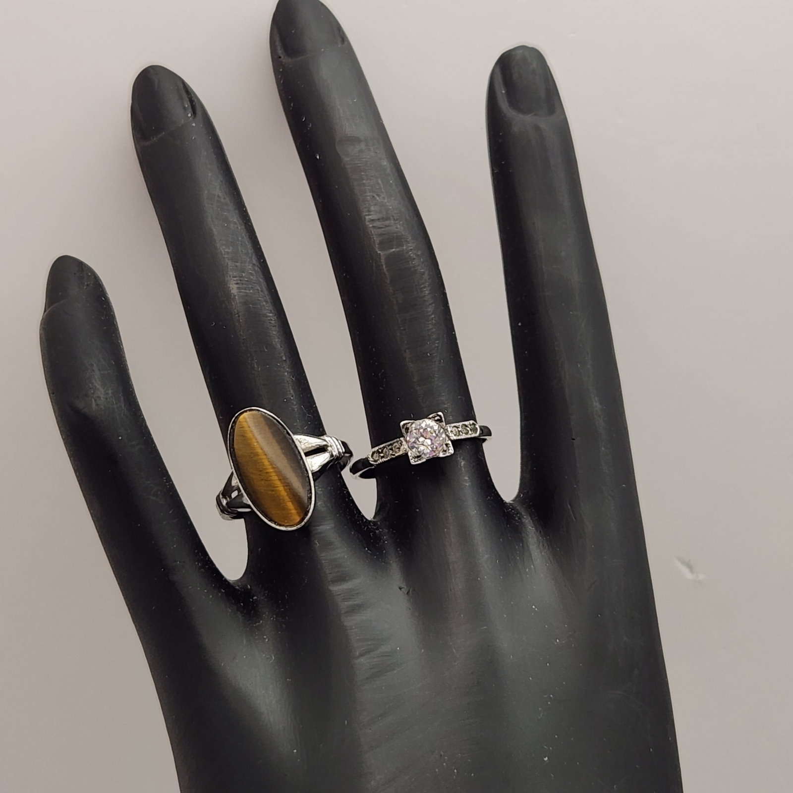 Sterling Gemstone Rings 4.2 Grams: One ring is bezel-set with an oval cabochon tiger's eye gemstone, while the other is an engagement-style ring with clear faceted stones in an elevated prong setting. Combined weight: 4.2 grams Tiger's