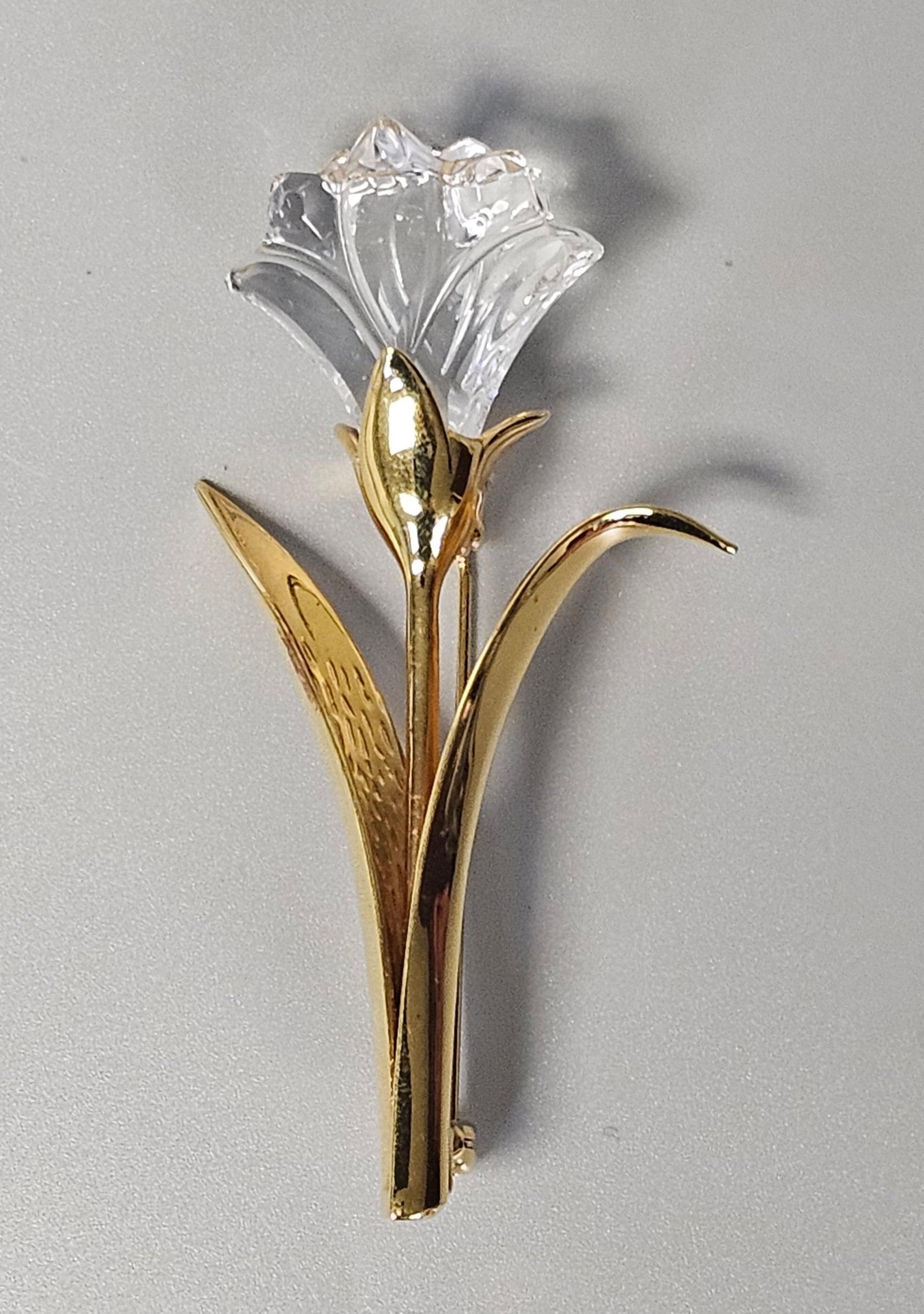Swarovski Crystal Lily Flower Brooch: A Swarovski gold-toned metal brooch designed as a single-stemmed lily flower. The piece features a multi-faceted clear crystal flower head set into a mounting with contrasting polished and
