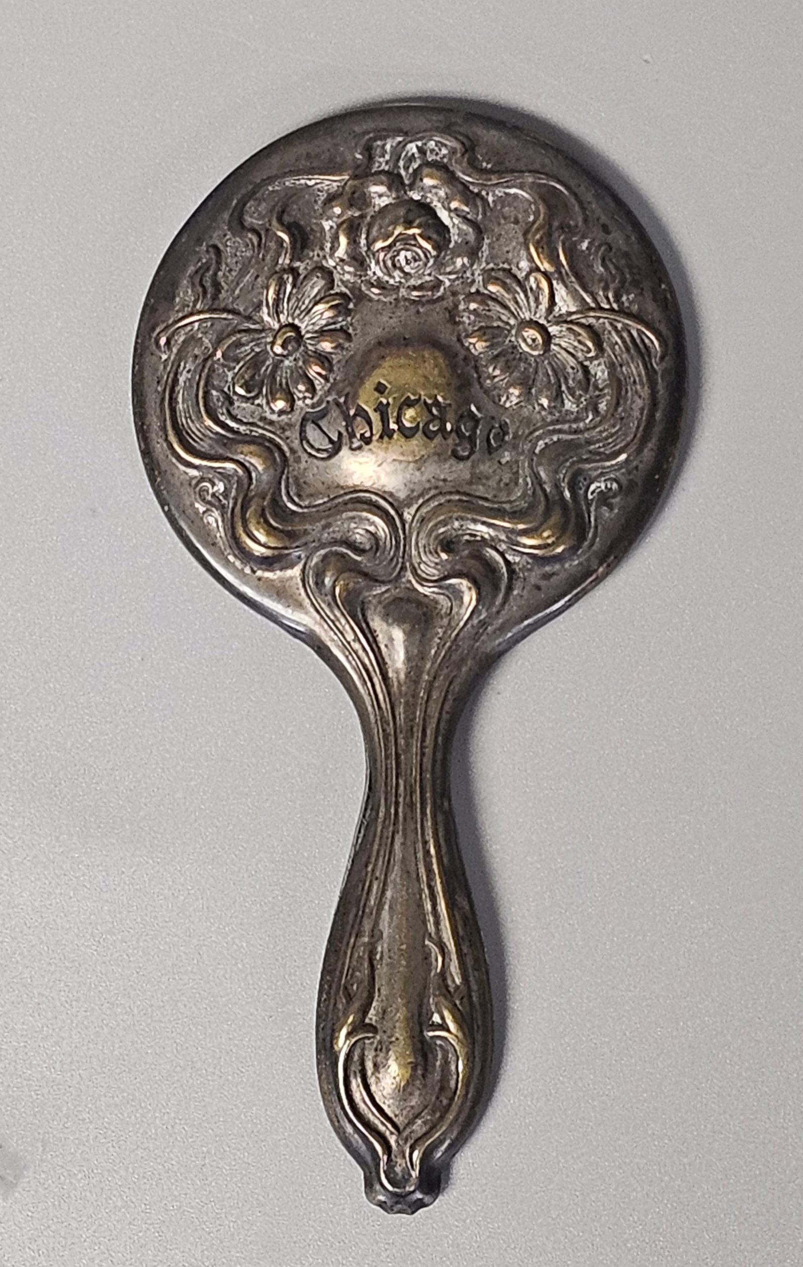 Art Nouveau Chicago Souvenir Mirror: This silver-plated base metal souvenir purse mirror features high-relief Art Nouveau floral motifs including roses and daisies with characteristic whiplash curves. The reverse is embossed with the wor