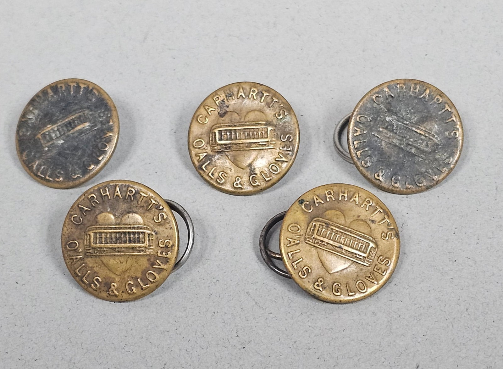 Vintage Carhartt Workwear Buttons: A set of five vintage workwear buttons featuring the early Carhartt Car-in-Heart trademark. Each button is embossed with a central trolley car within a heart, surrounded by the text CARHARTT'S O'ALLS 