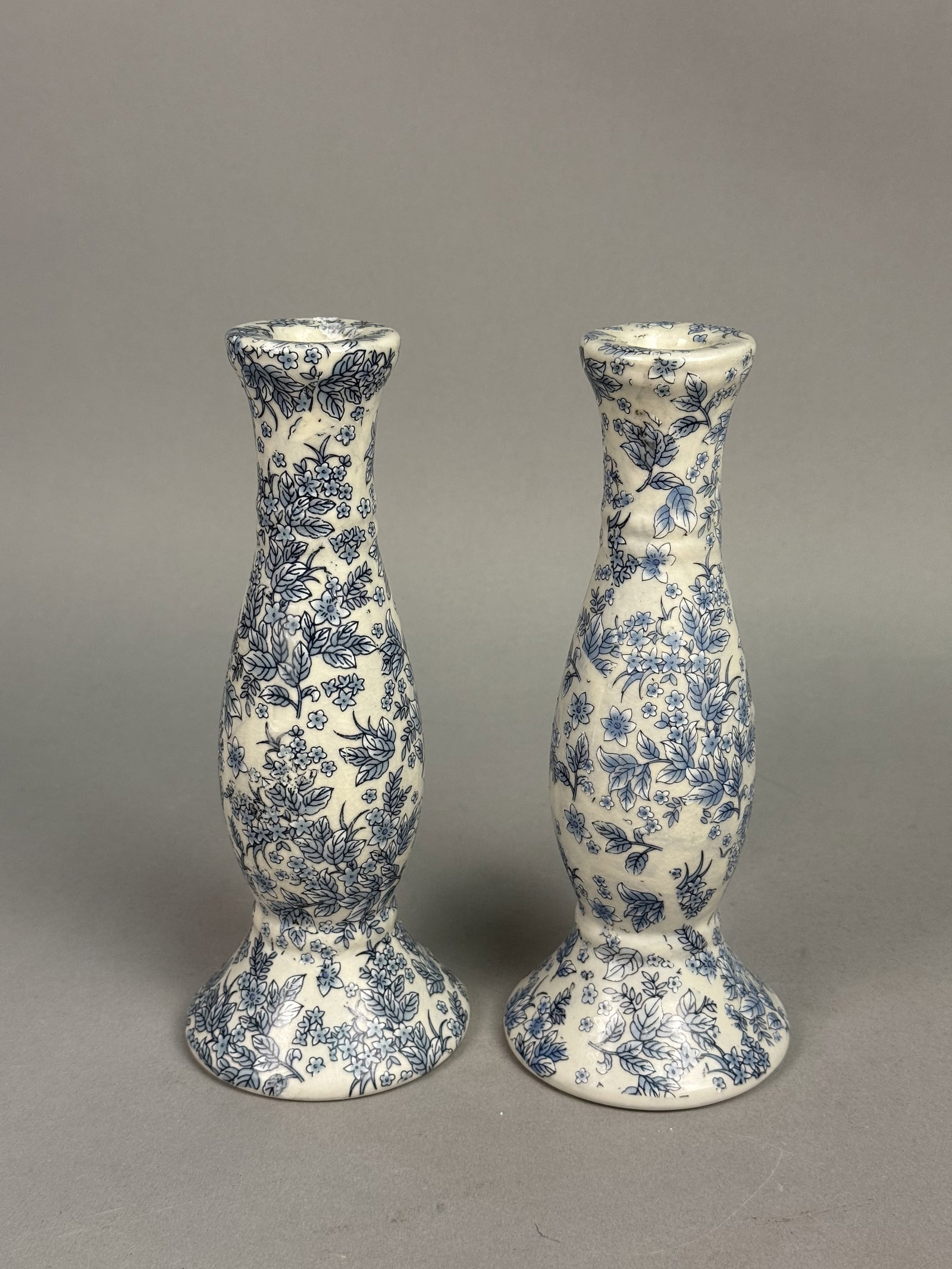 Pair of Orchid Brand Candlesticks: A pair of baluster-form earthenware candlesticks by Orchid Brand, featuring an all-over blue transfer-printed floral chintz design. Each piece is constructed with a flared circular base and a lipped r