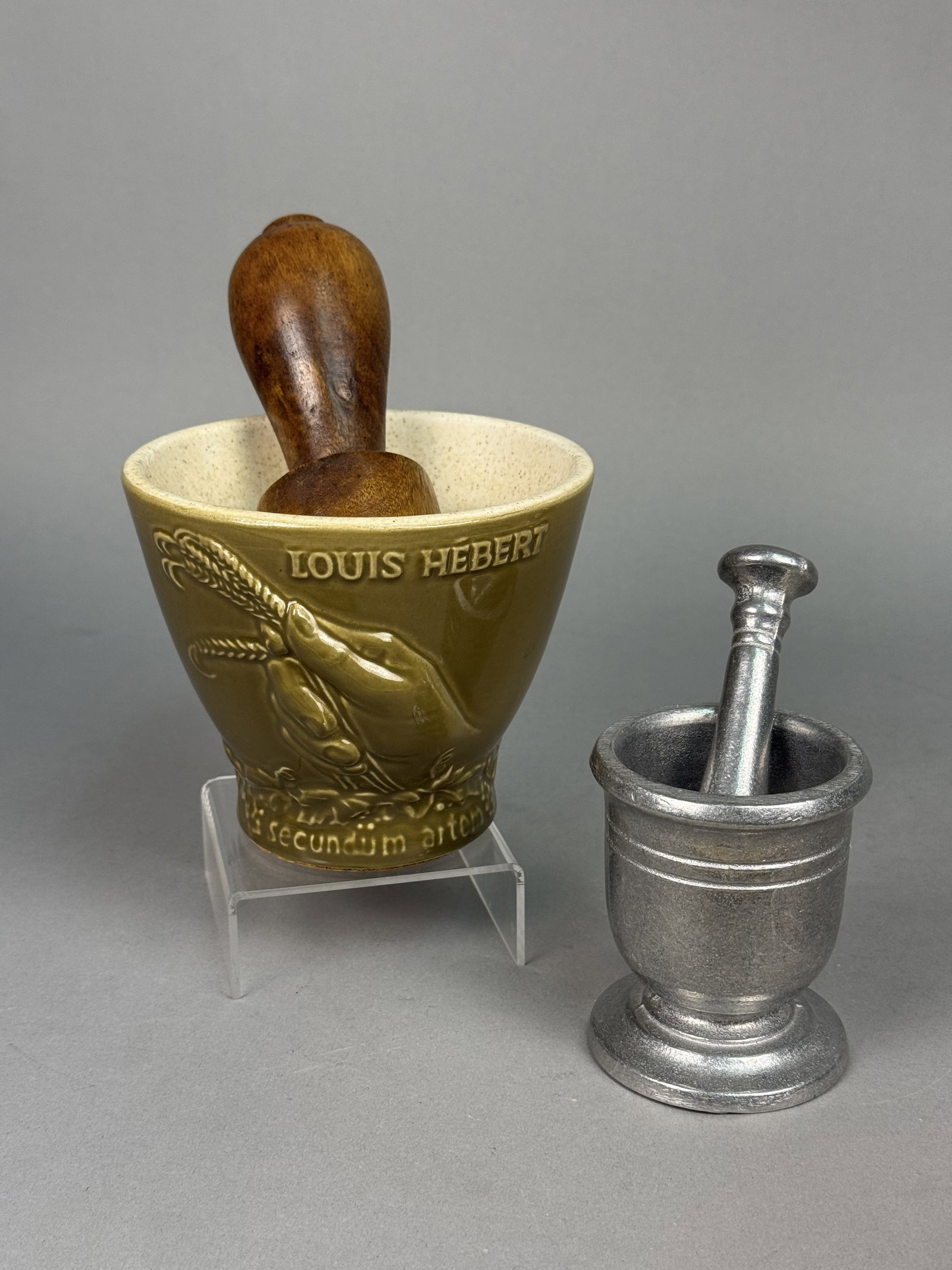 Two Pharmaceutical Mortar and Pestle Sets: This lot features a commemorative Schering Corporation ceramic mortar and wooden pestle alongside a smaller metal set. The glazed ceramic mortar displays molded relief work honoring Louis Hebert with