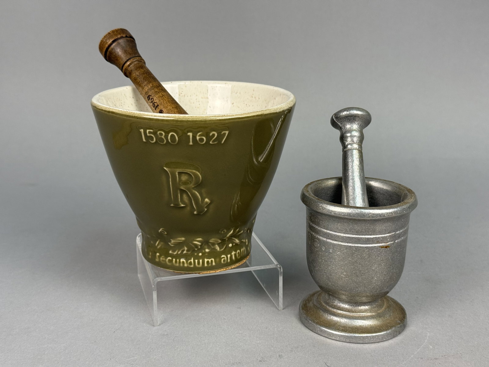 Two Pharmaceutical Mortar and Pestle Sets: The first set includes a glazed ceramic mortar honoring Louis Hebert with relief inscriptions reading 1580 1627 and secundum artem, paired with a turned wood pestle branded for Coricidin 1949-1969.