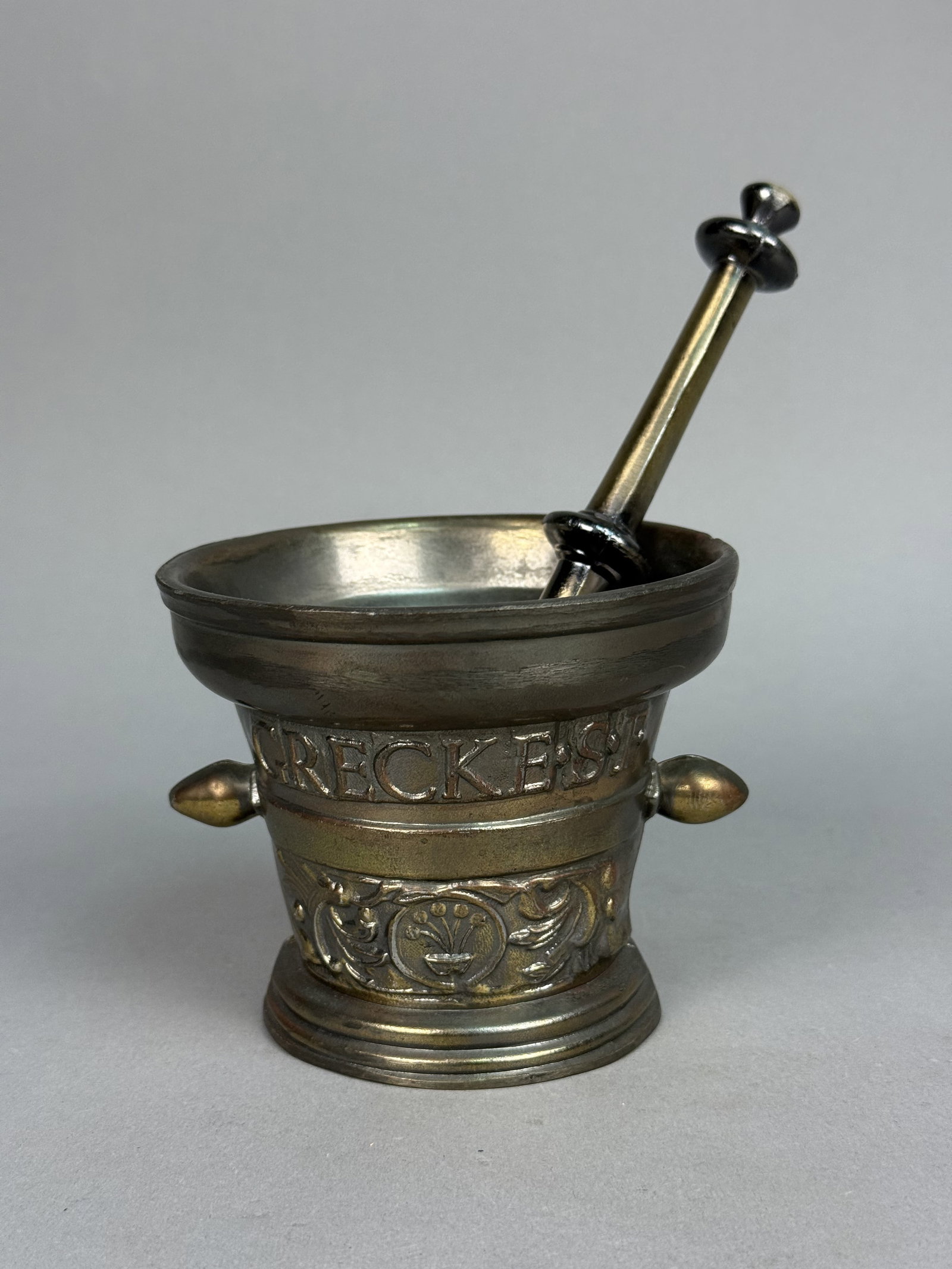 Richard Klein Bronze Mortar and Pestle: This cast bronze mortar and matching pestle were produced by Richard Klein, bearing the R.A.K. 1 mark on the base. The body features high-relief decoration including a lower register of stylized folia