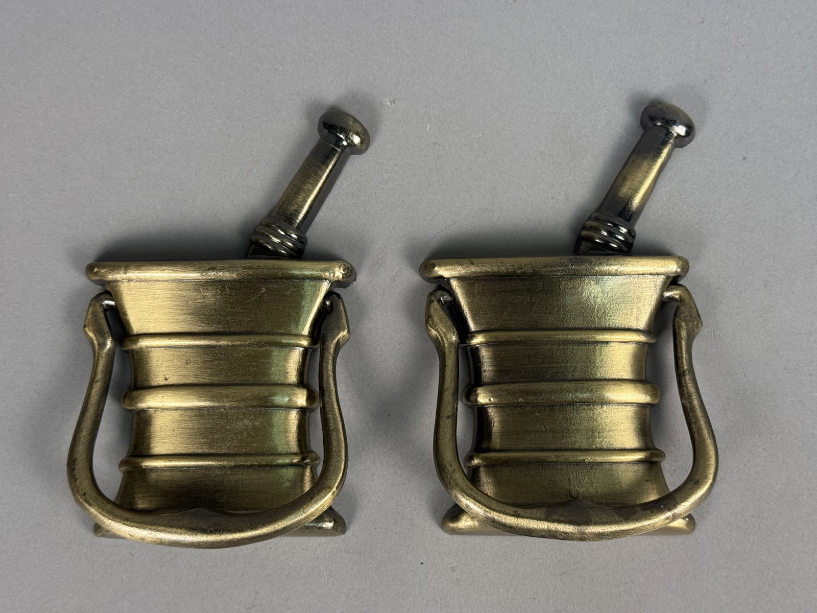 Pair of Brass Apothecary Door Knockers: This pair of cast brass door knockers is modeled after a traditional apothecary mortar and pestle. Each unit consists of a static vessel and pestle with a separate swinging bail handle and an antiqued