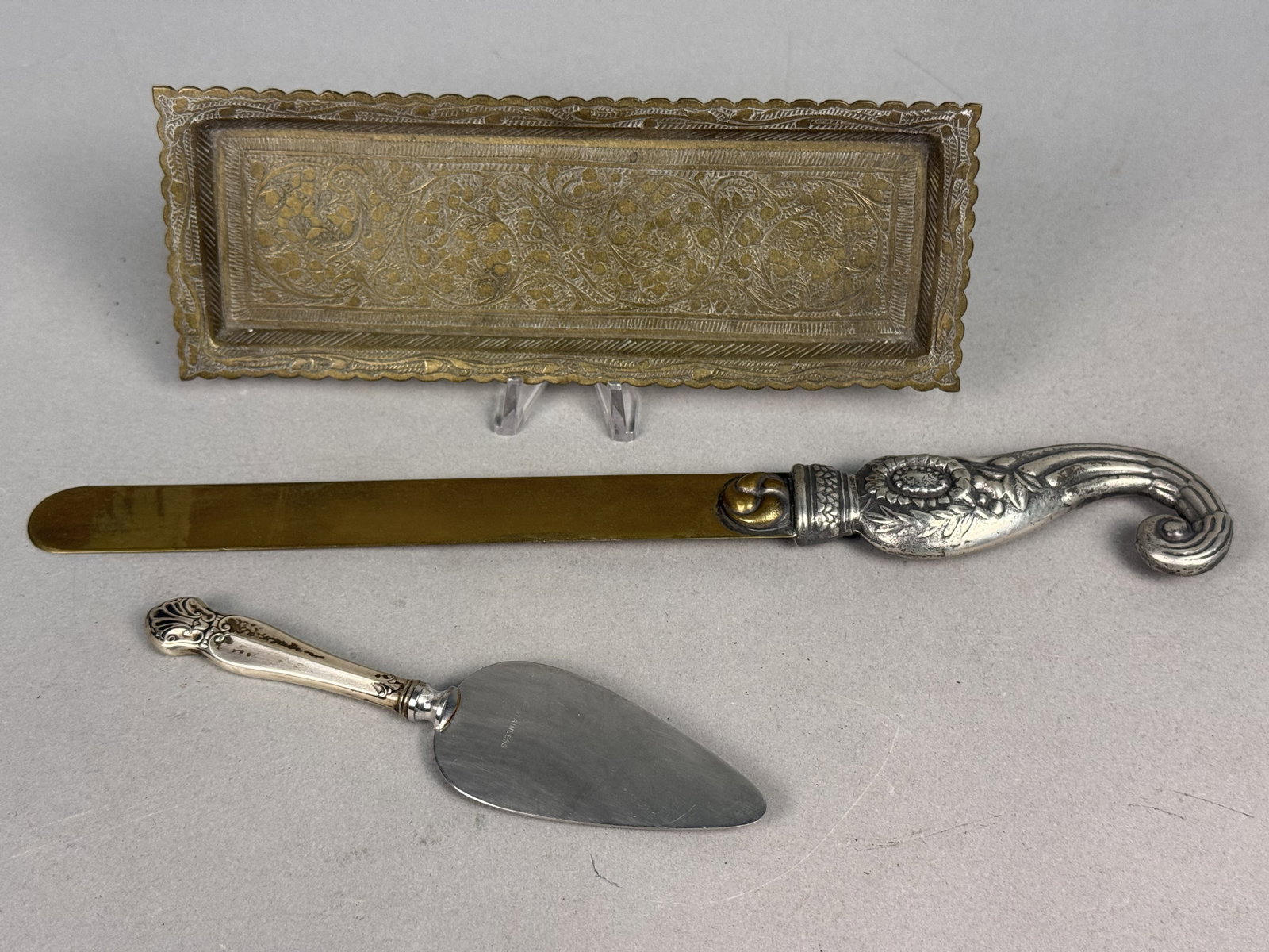 Trio of Vintage Decorative Metalware: This assortment includes a rectangular brass tray, an ornate letter opener, and a small server. The tray features hand-chased floral scrollwork and is marked Made in India on the reverse. The letter o