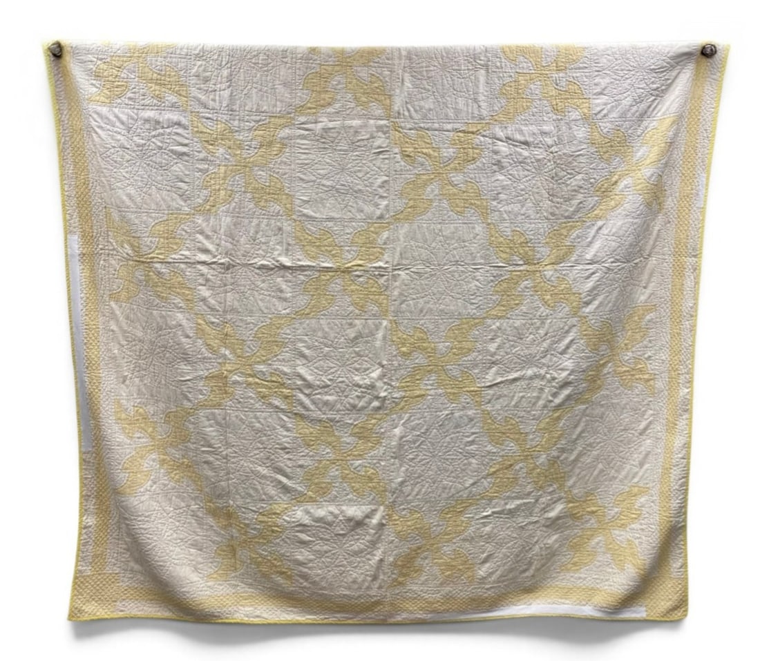 American Foliate Applique Cotton Quilt: This hand-stitched and appliqued cotton quilt features a repeating four-lobed foliate pattern in pale yellow set against a white ground. The construction showcases dense hand-quilting with motifs