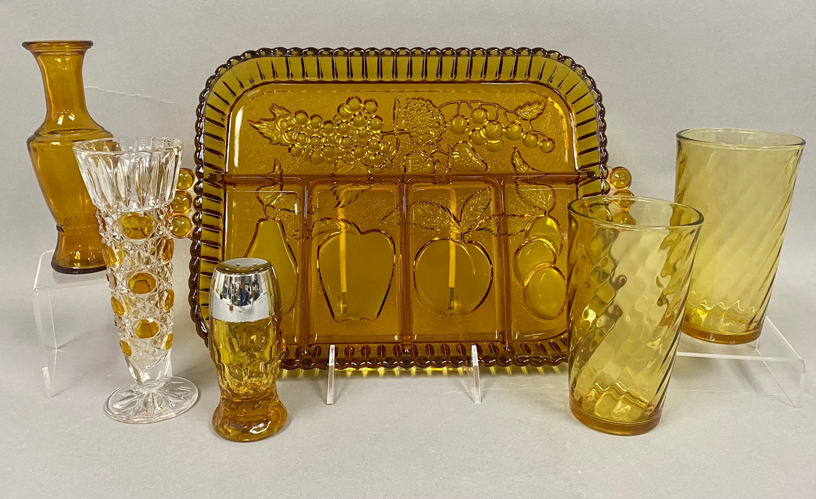 Collection of Mid-Century Amber Glassware: This collection of vintage amber and decorative glassware features an Indiana Glass divided serving tray in the Fruit pattern with embossed orchard motifs and beaded handles. Included is a clear press