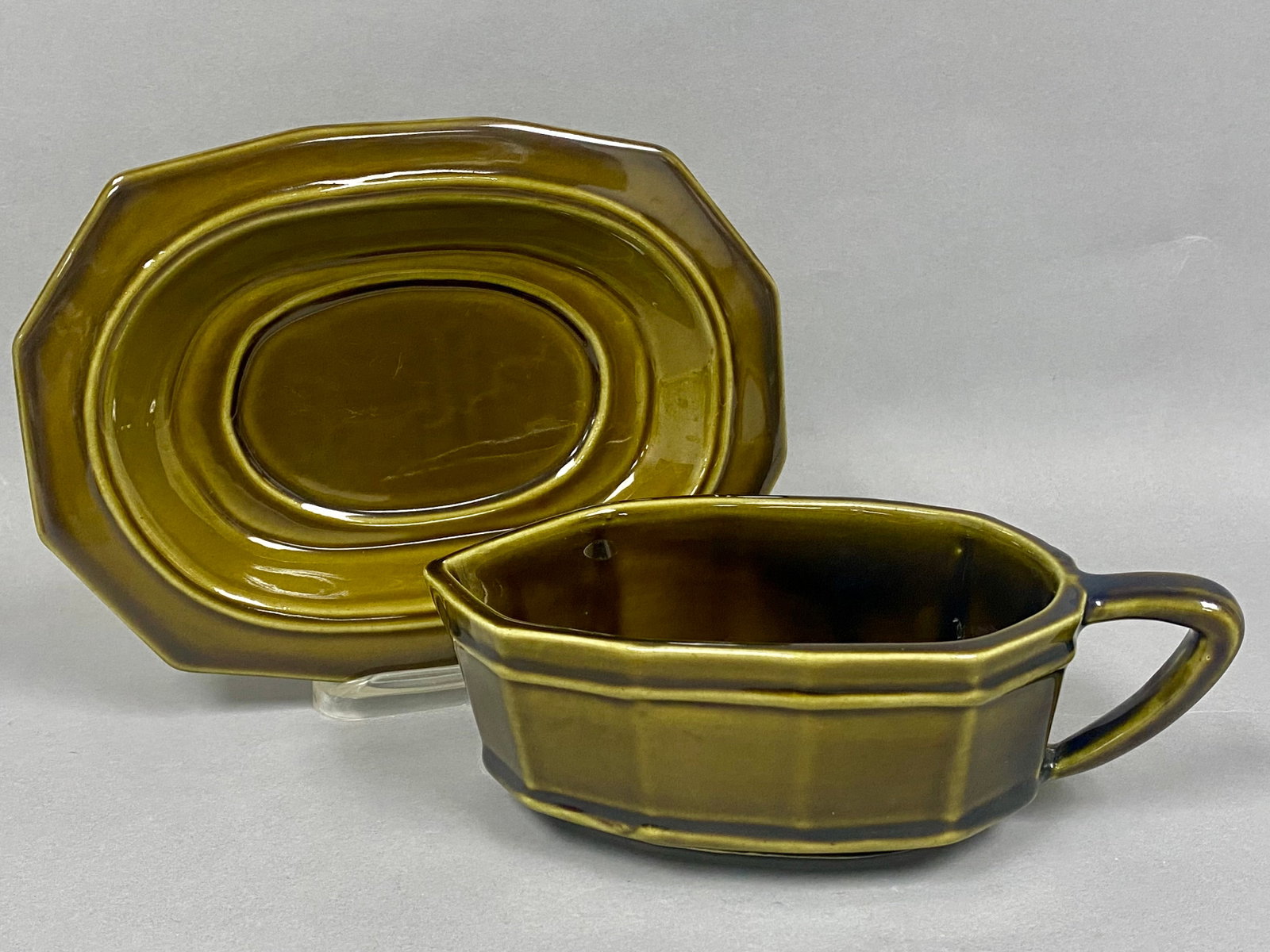Two-Piece Pfaltzgraff Heritage Green Server: This Pfaltzgraff Heritage Green sauce boat and matching underplate were designed by Georges Briard and feature a faceted, octagonal profile. The ceramic stoneware set is finished in a high-gloss
