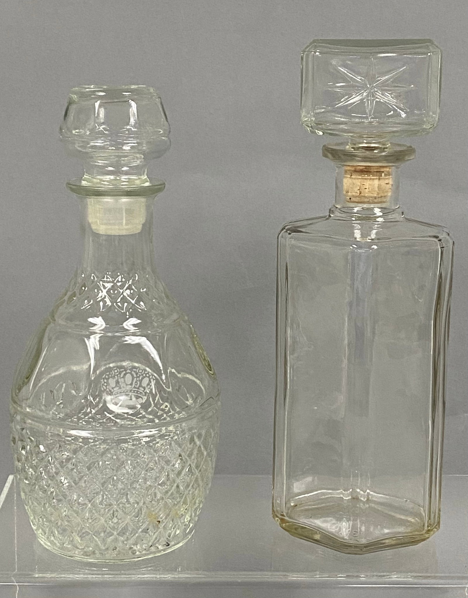 Two Vintage Clear Glass Decanters: This lot consists of two clear glass decanters of differing silhouettes. One features a bulbous body with diamond-cut accents and a frosted crown motif, while the other is a rectangular bottle with