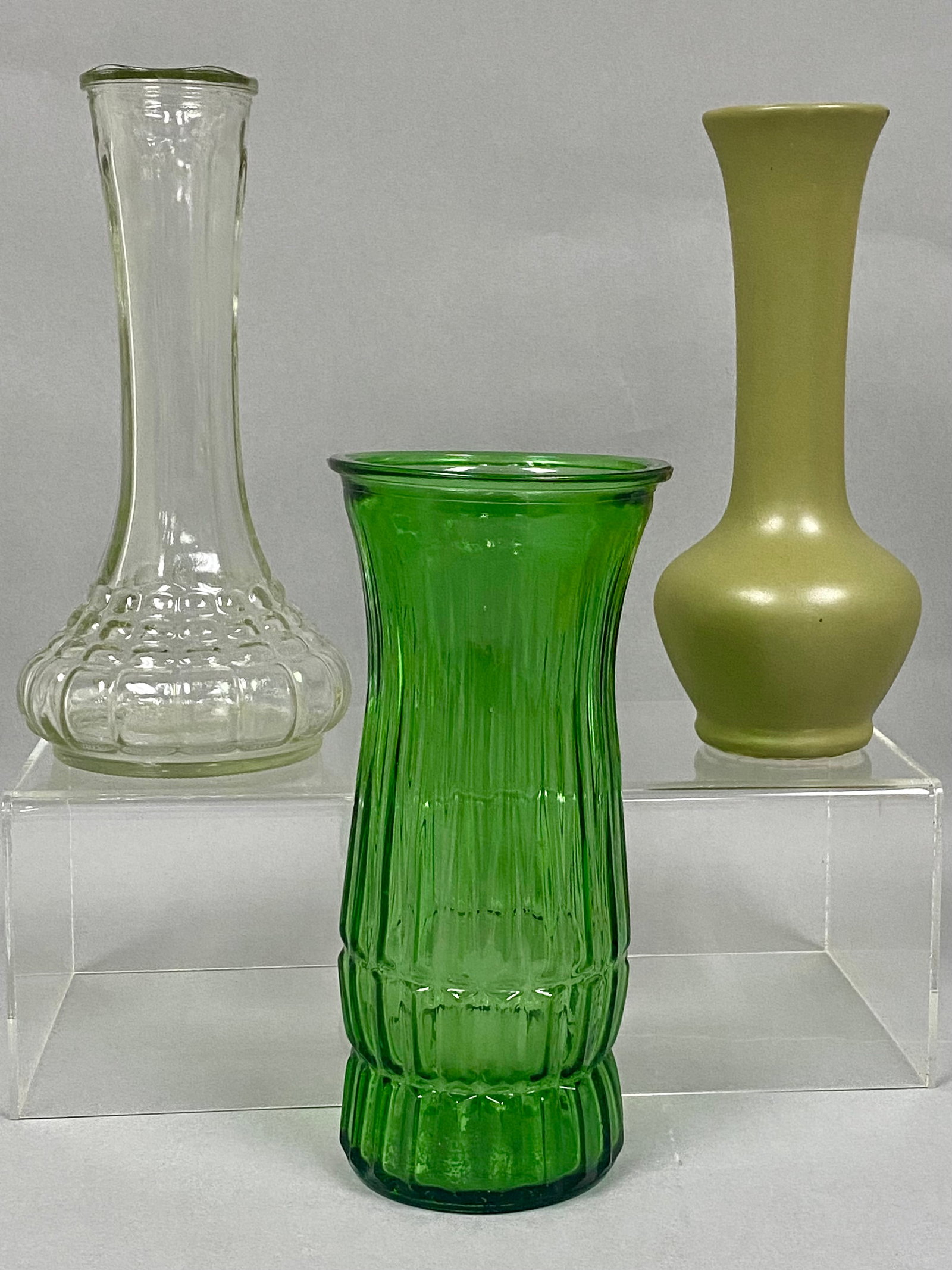 Trio of Mid-Century Florist Vases: This collection includes three mid-century modern florist vases in glass and ceramic. The group features an emerald green ribbed glass vase by E.O. Brody Co., a clear glass vase with a textured block 