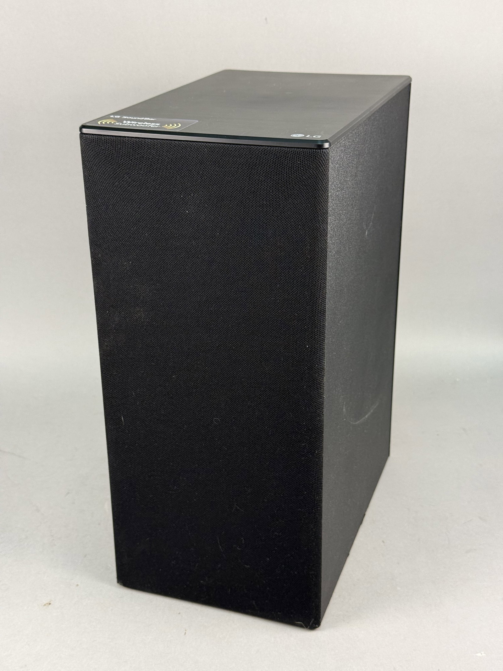 LG Wireless Active Subwoofer SPN5B-W: This LG wireless active subwoofer, model SPN5B-W, features a black cabinet with a front fabric grille and a rear-firing bass port. The unit is equipped with a pairing button and a two-prong AC power